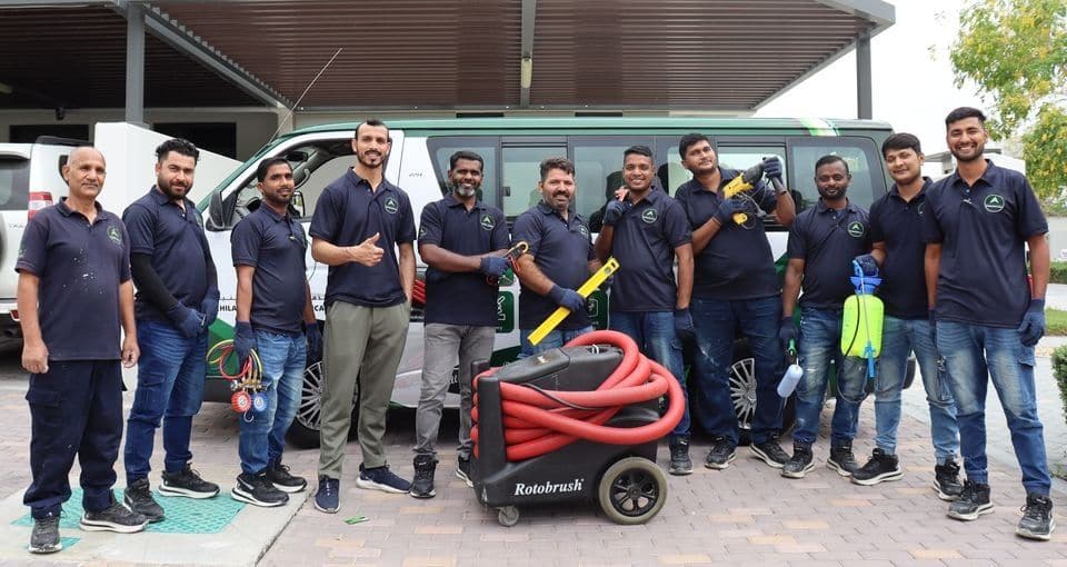 Twelve Al-Hilal Al-Thahabi technicians in company polo shirts beside a company van, holding their tools
