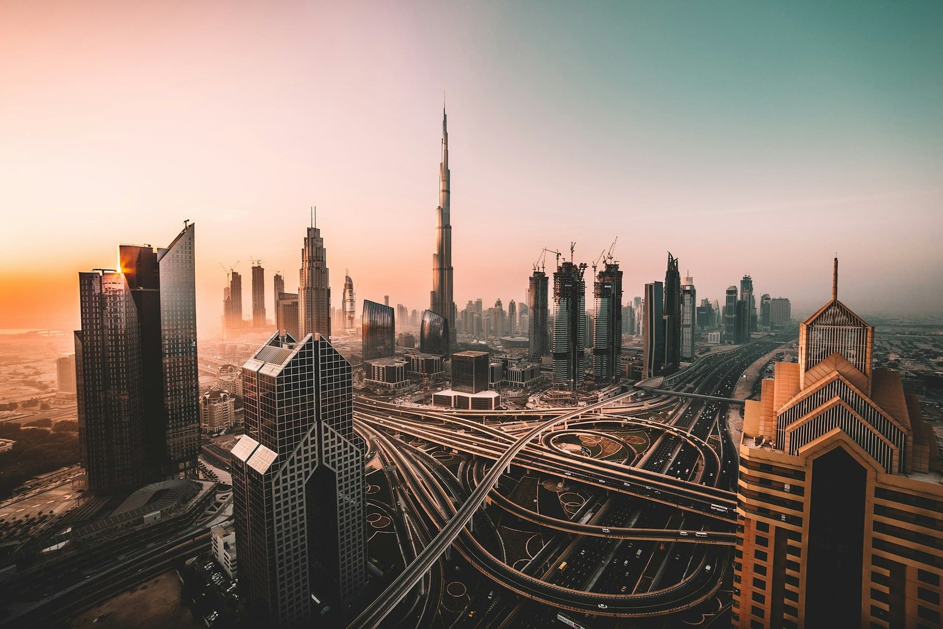 Burj Khalifa and Downtown Dubai towers above a busy highway interchange at sunset