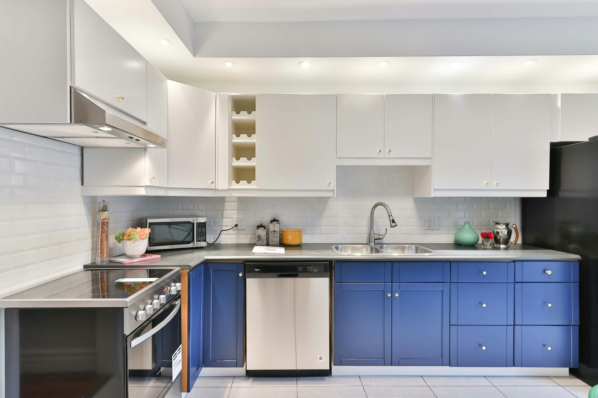 Kitchen with royal-blue base cabinets, white wall units, a white tile backsplash and a stainless dishwasher