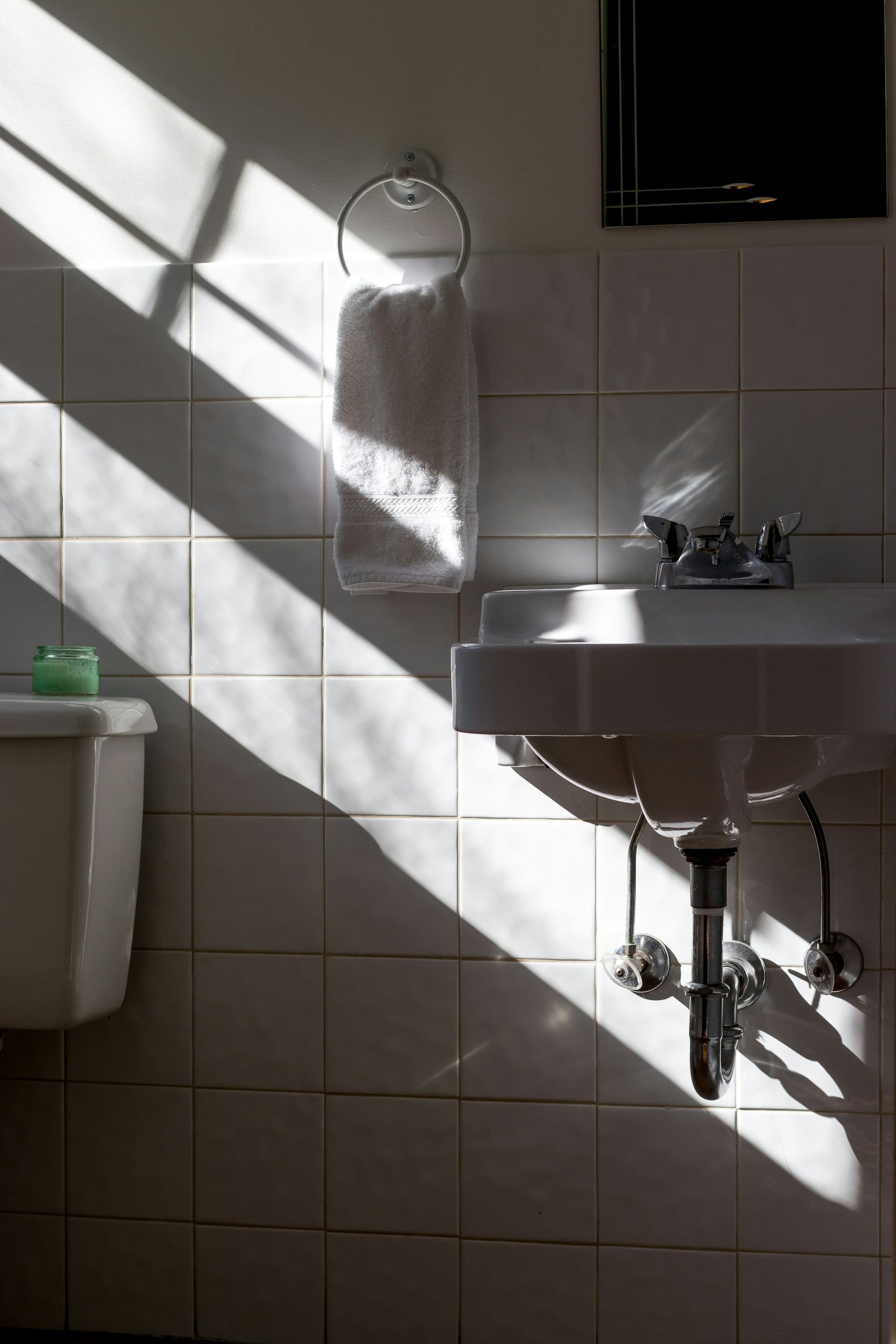 A wall-hung basin in a tiled bathroom, with its trap and shut-off valves exposed beneath