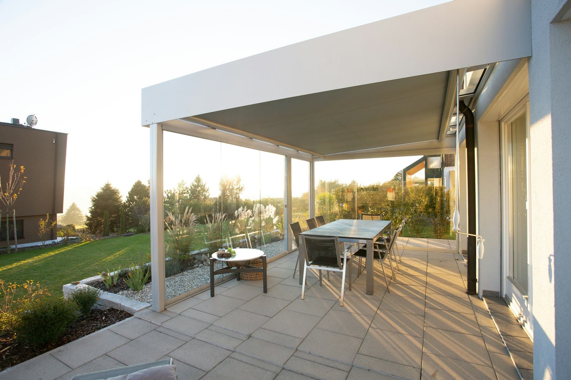 Stone-paved patio under a white flat roof with a dining table in low evening sun
