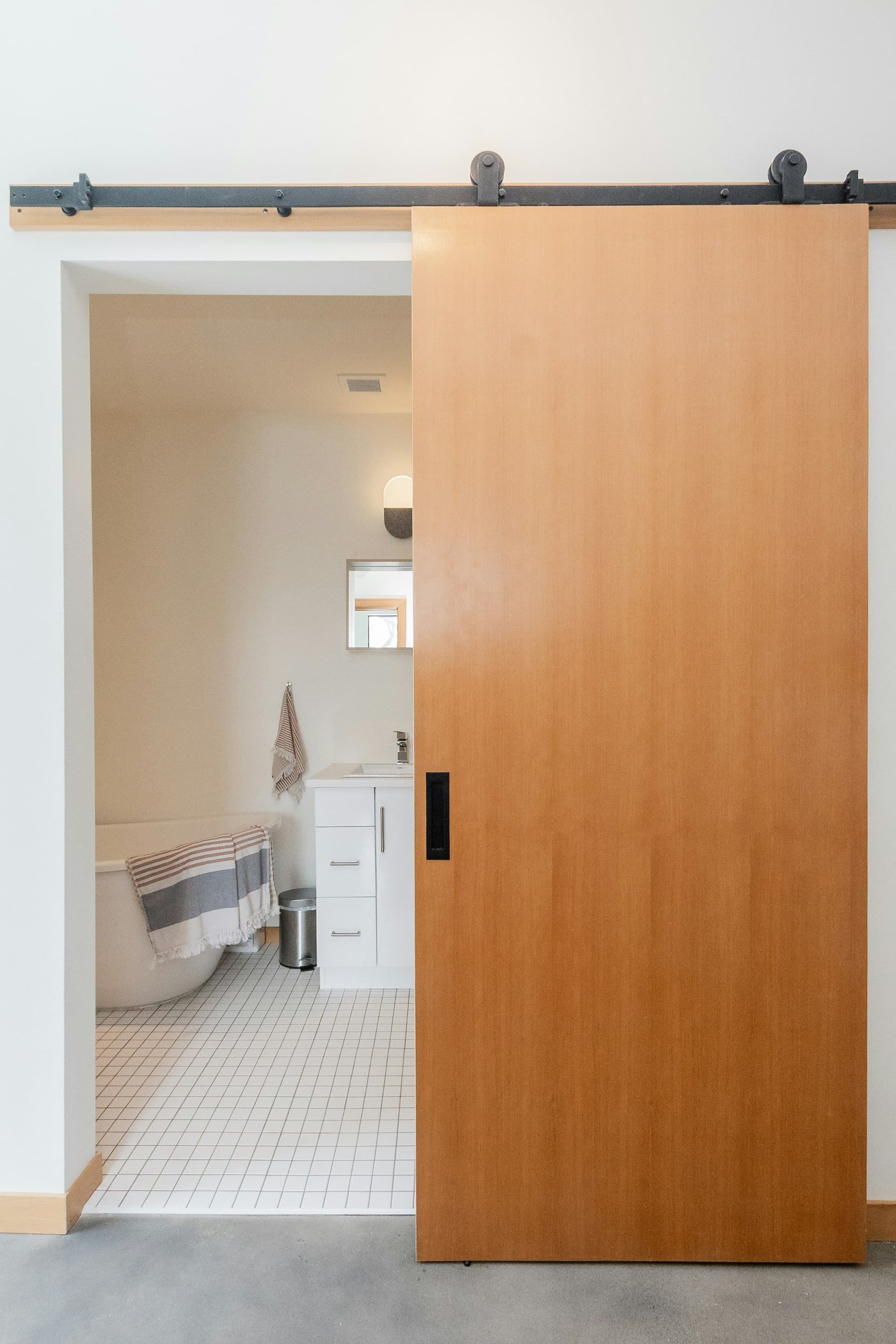 Oak sliding door on a black overhead track opening onto a bathroom