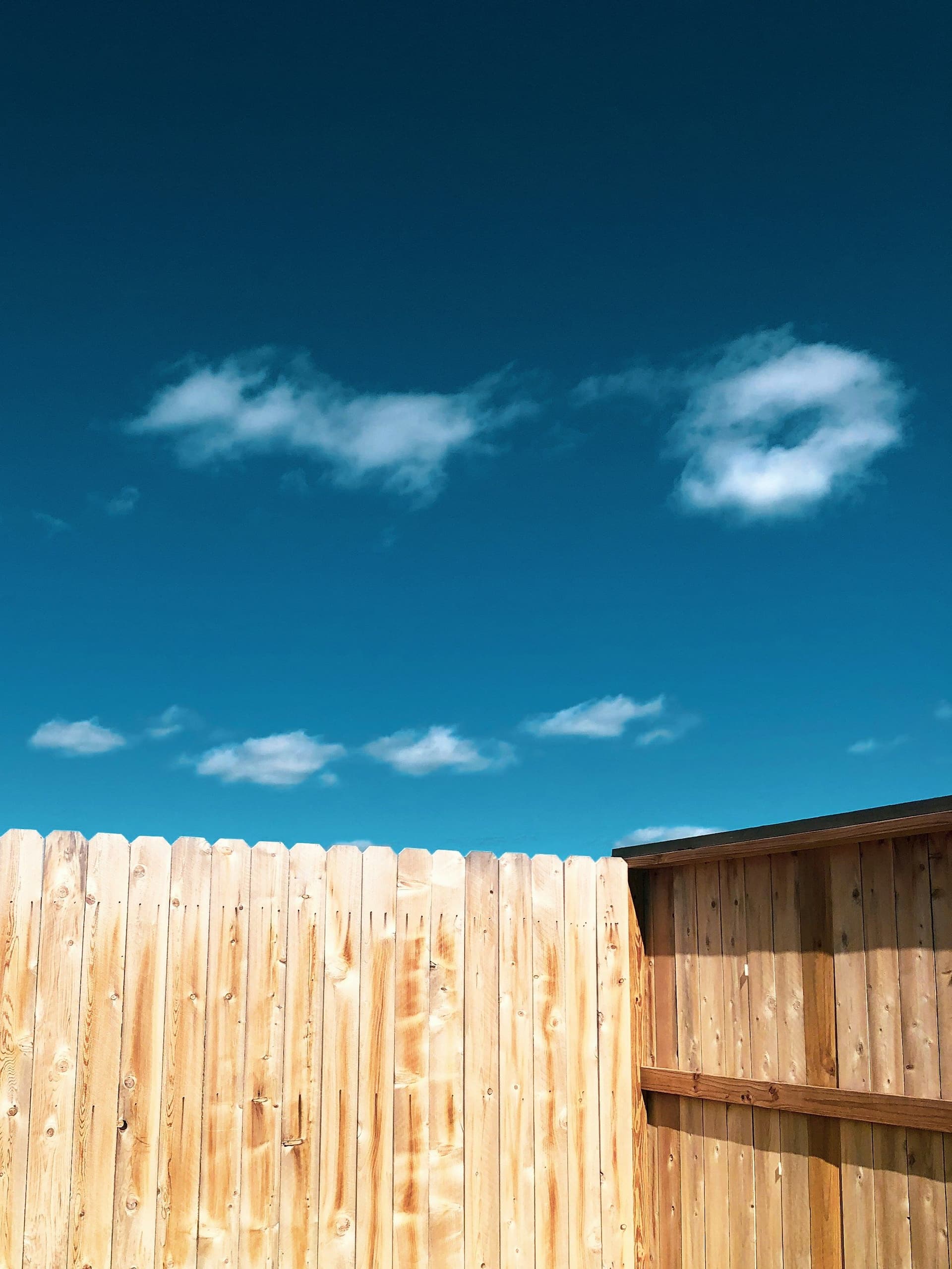 Light wooden plank fence against a deep blue sky with small white clouds