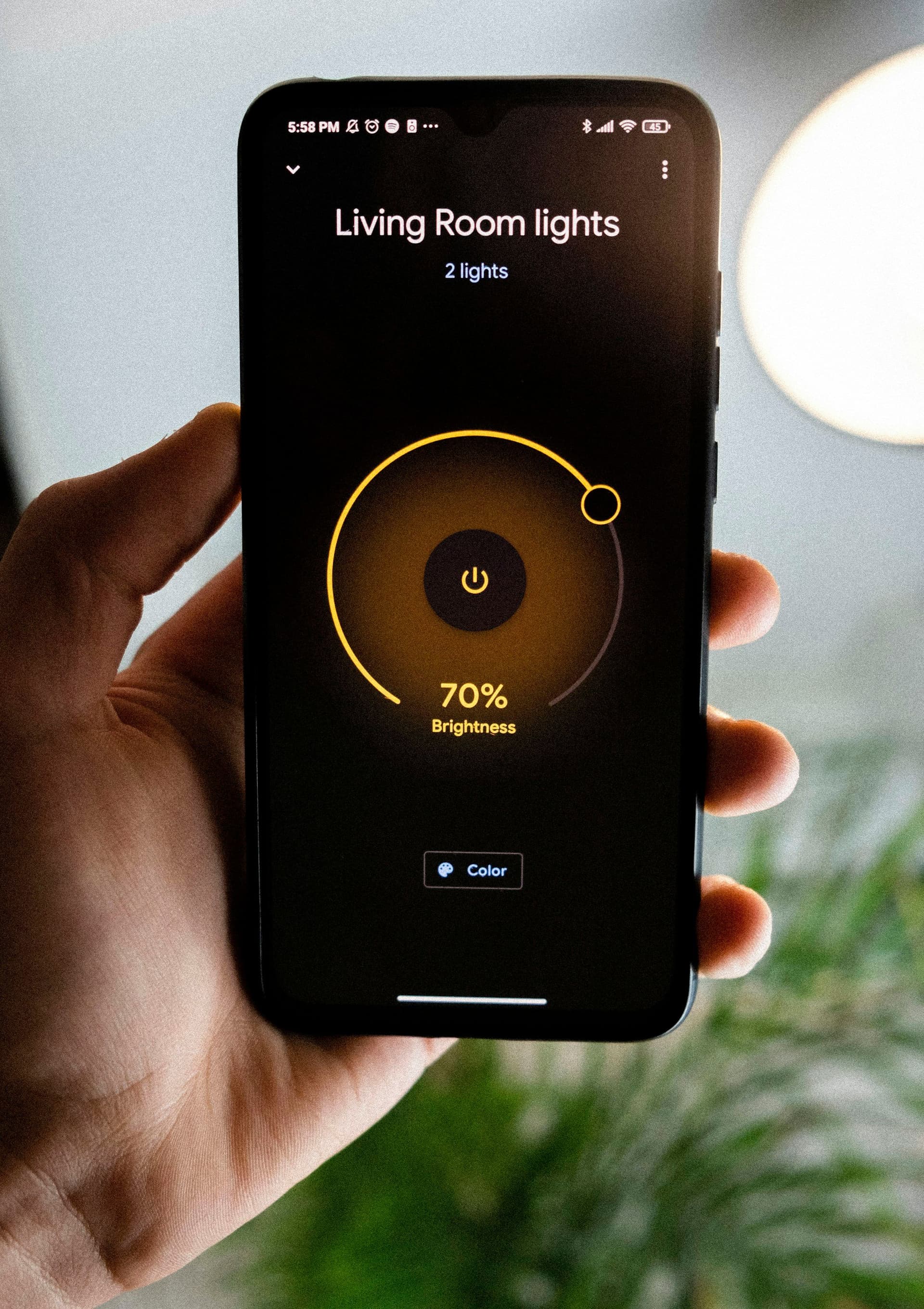 A hand holds a phone showing a living room lights screen with a brightness dial