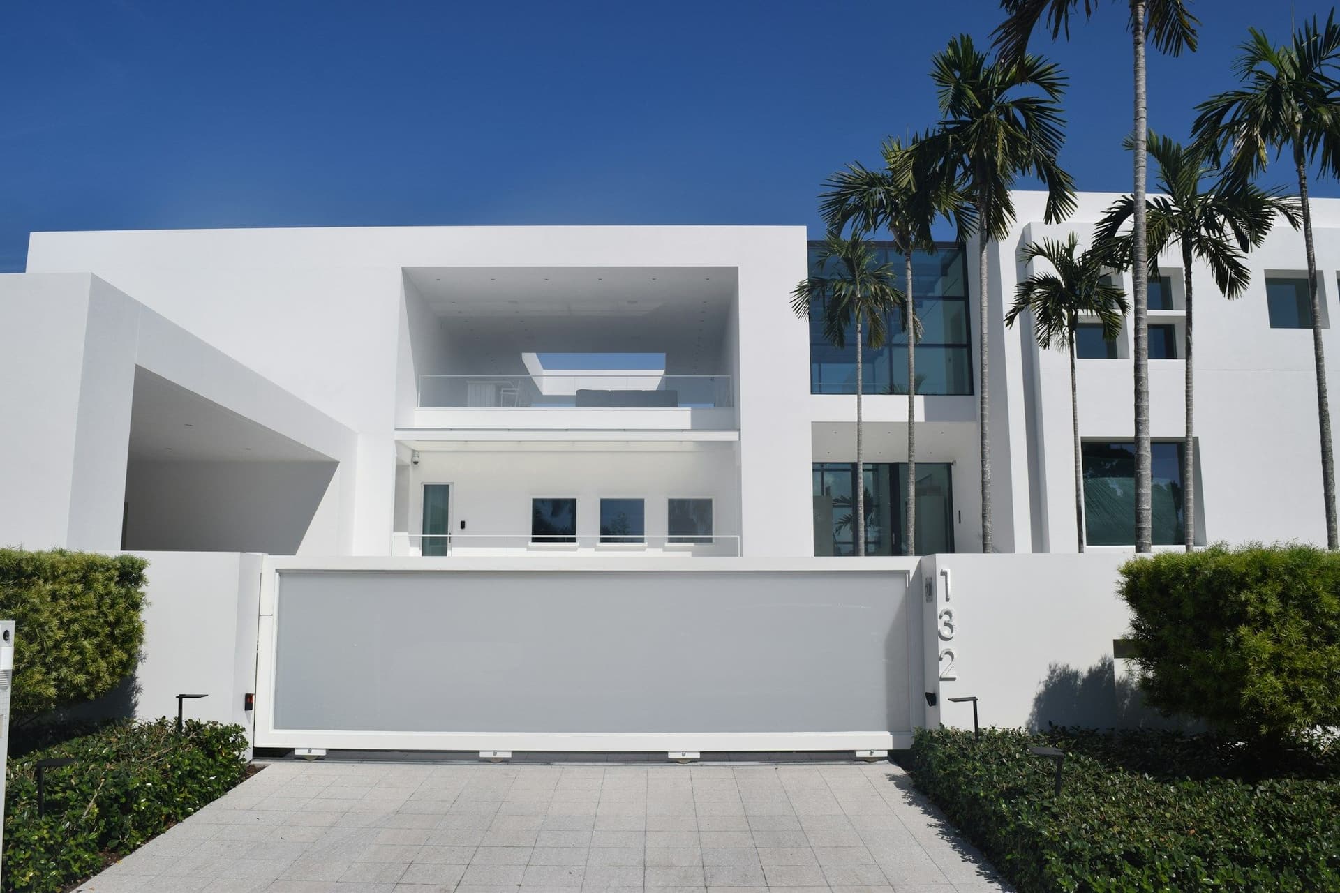 White modern villa with palm trees behind a white sliding gate and a block-paved driveway
