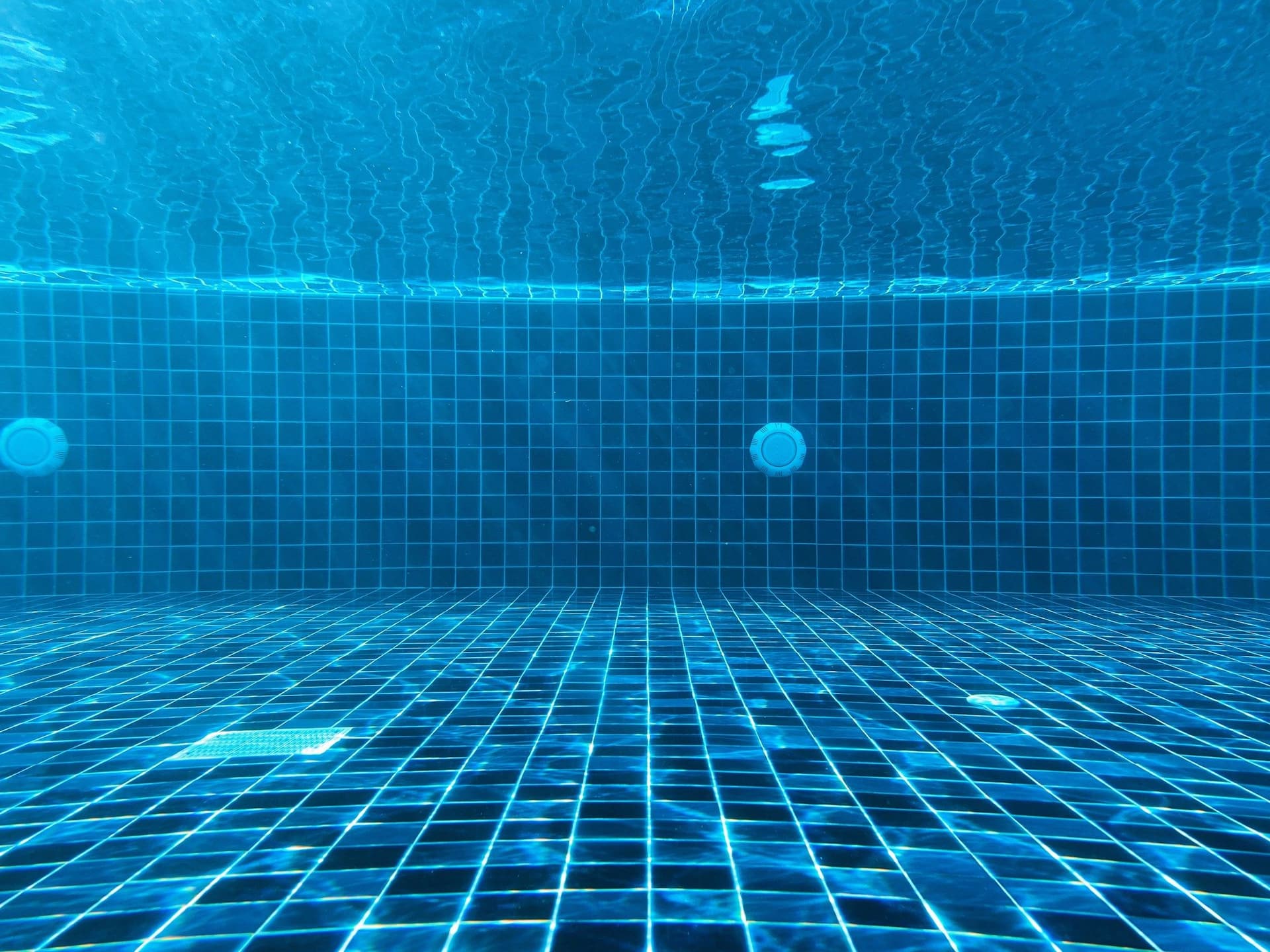 Underwater view of a blue-tiled pool floor and wall with round lights and a floor drain