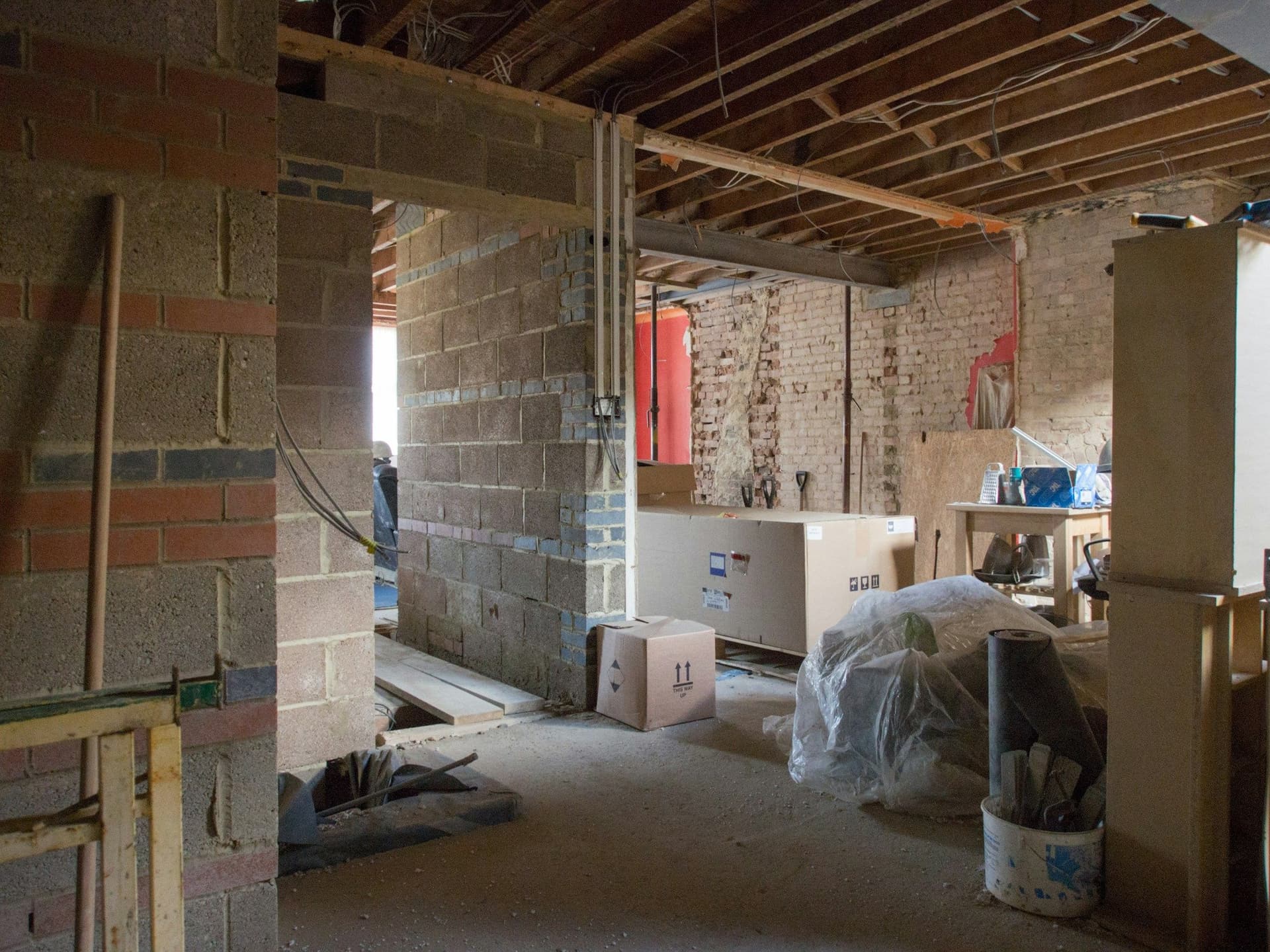 A wide opening between two rooms in a house under renovation, with block piers either side and exposed joists overhead
