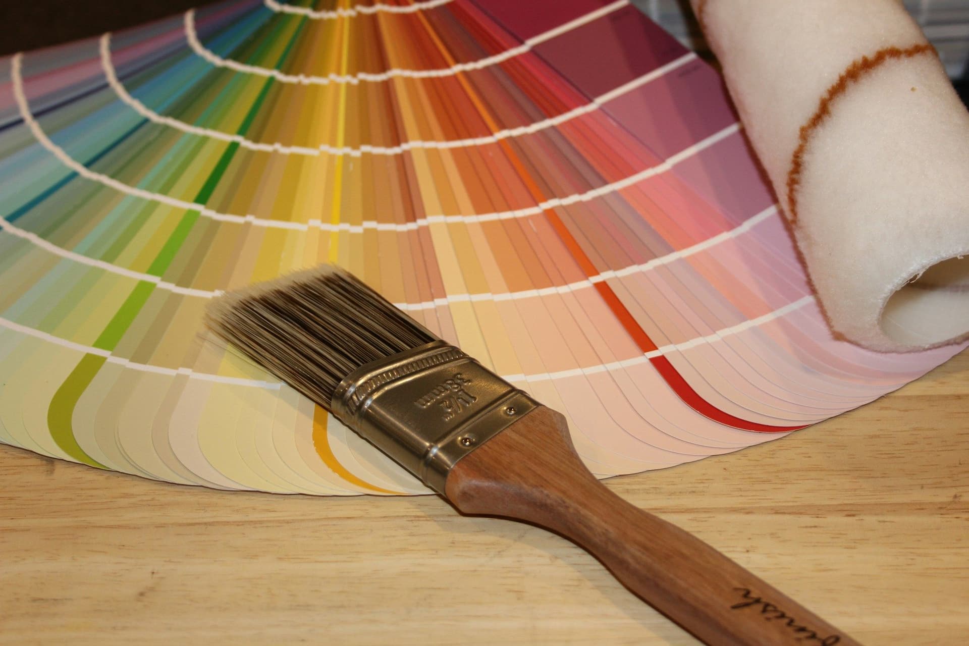 Paint brush and roller lying across a fan of paint color swatches on a wooden table