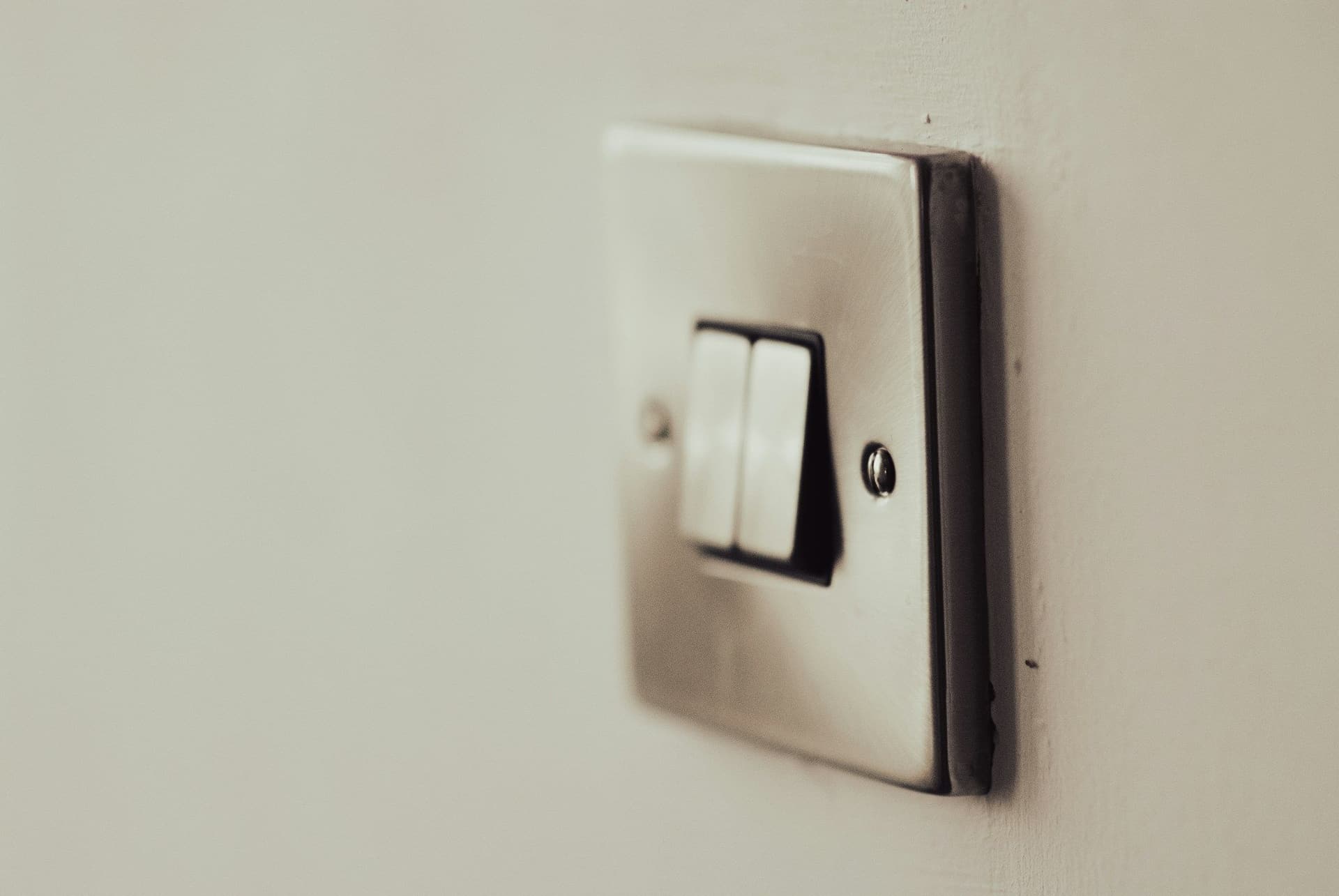 White two-gang light switch with a brushed metal plate on a pale wall