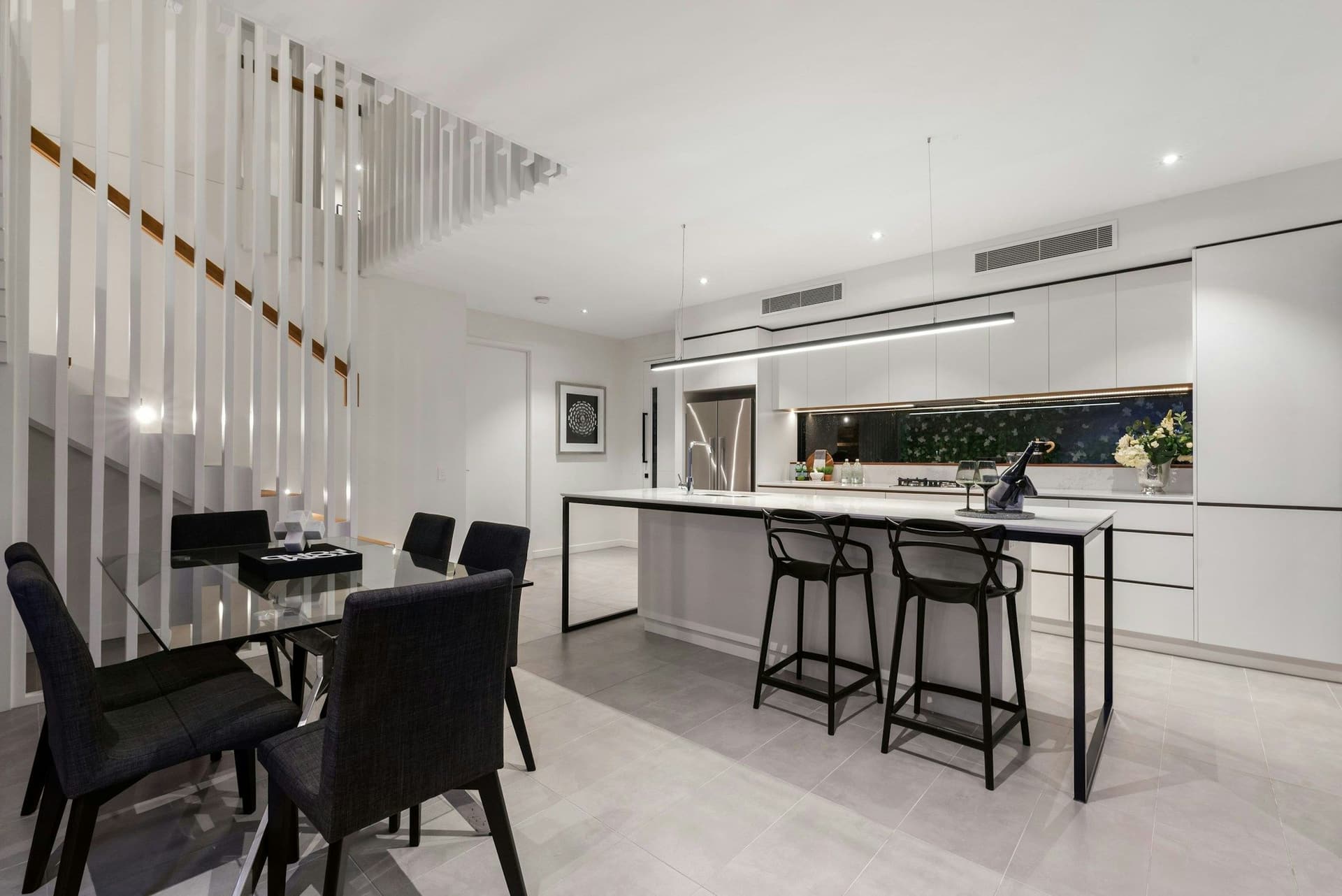 Open-plan kitchen and dining area with a long island, black bar stools and a staircase with a slatted screen