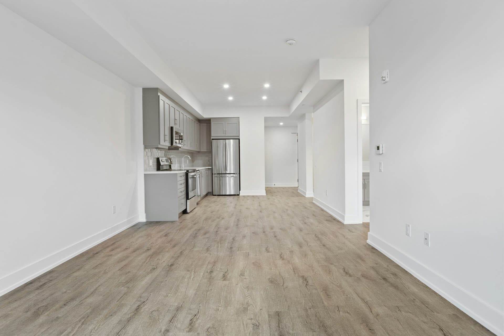 Empty open-plan apartment with a wood-look floor running from the living area to a kitchen at the far end