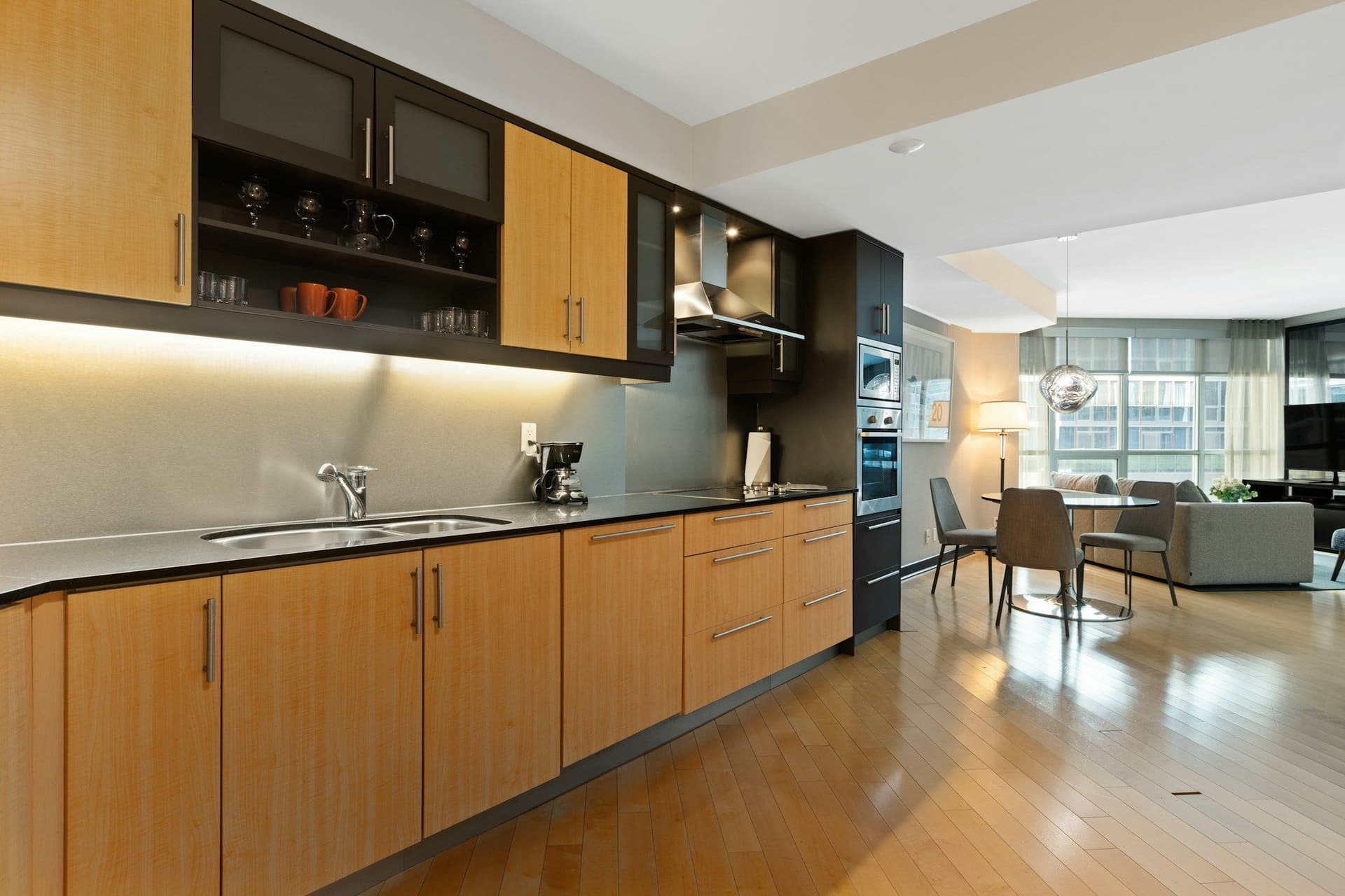 Long kitchen run in warm wood-grain cabinets with a dark countertop, open to a dining area