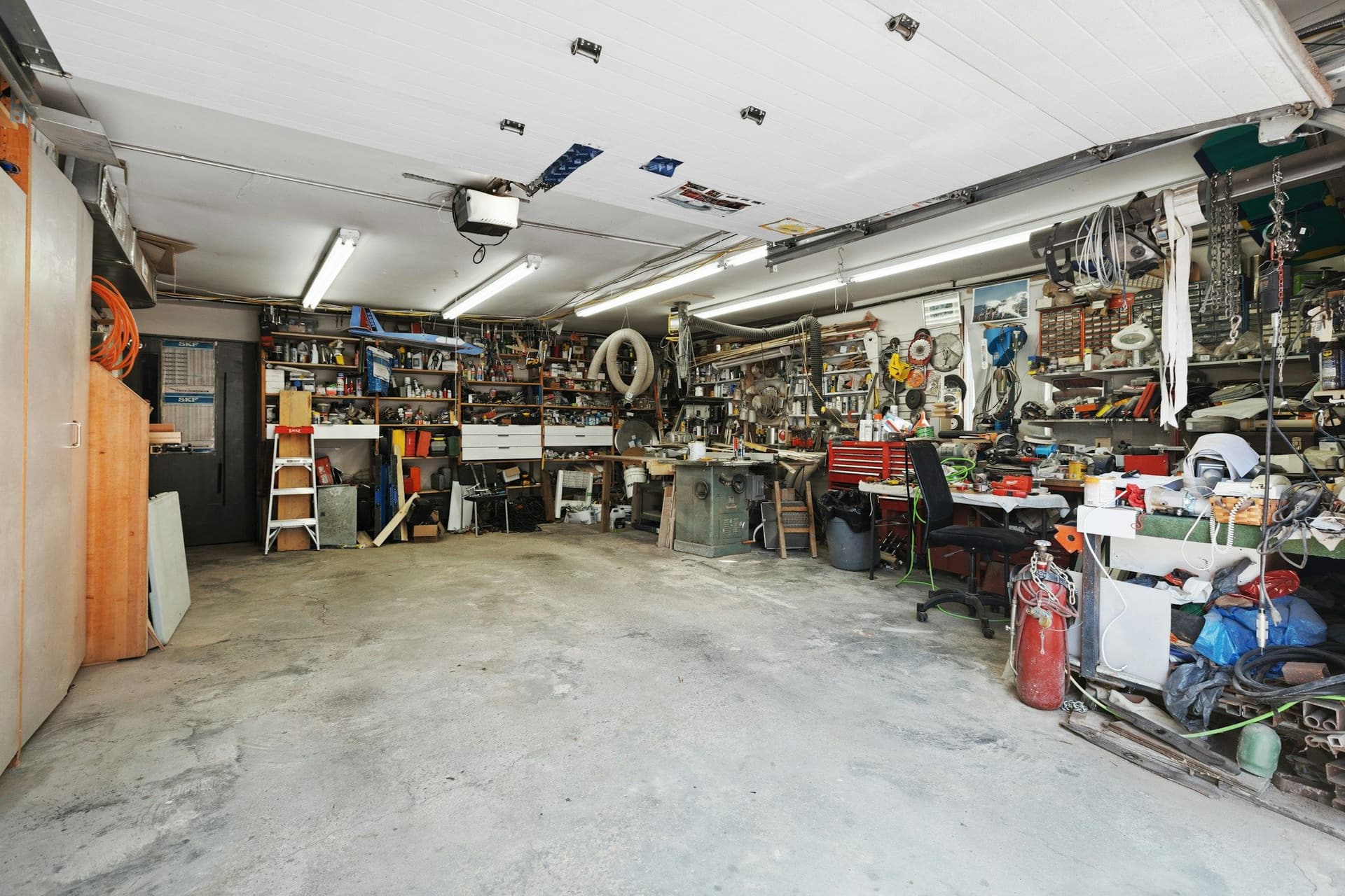 A garage with a bare concrete floor and shelves, workbenches and tools packed along the walls