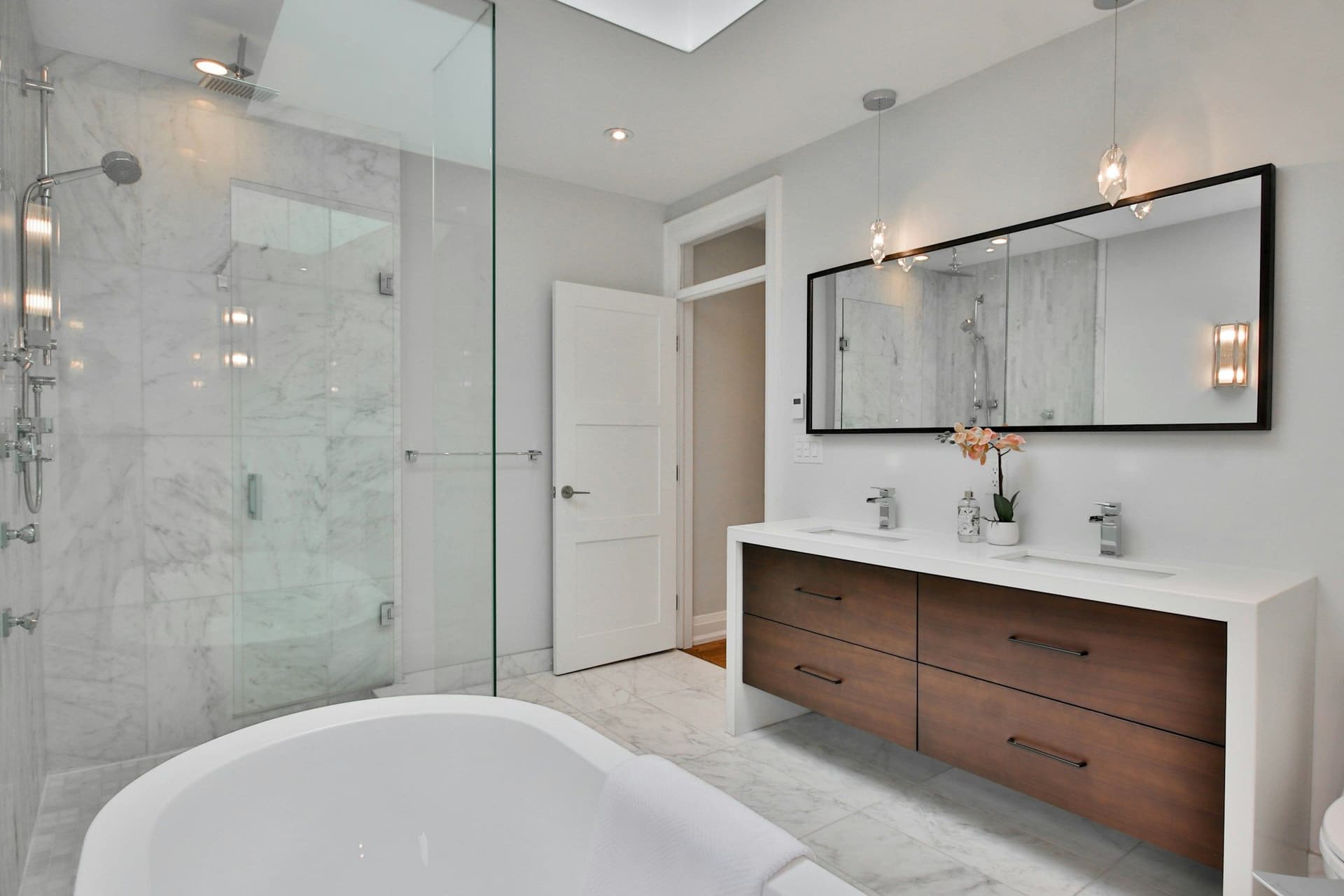 Bathroom with a floating wood vanity, a large mirror, a white bath and a glass-enclosed shower
