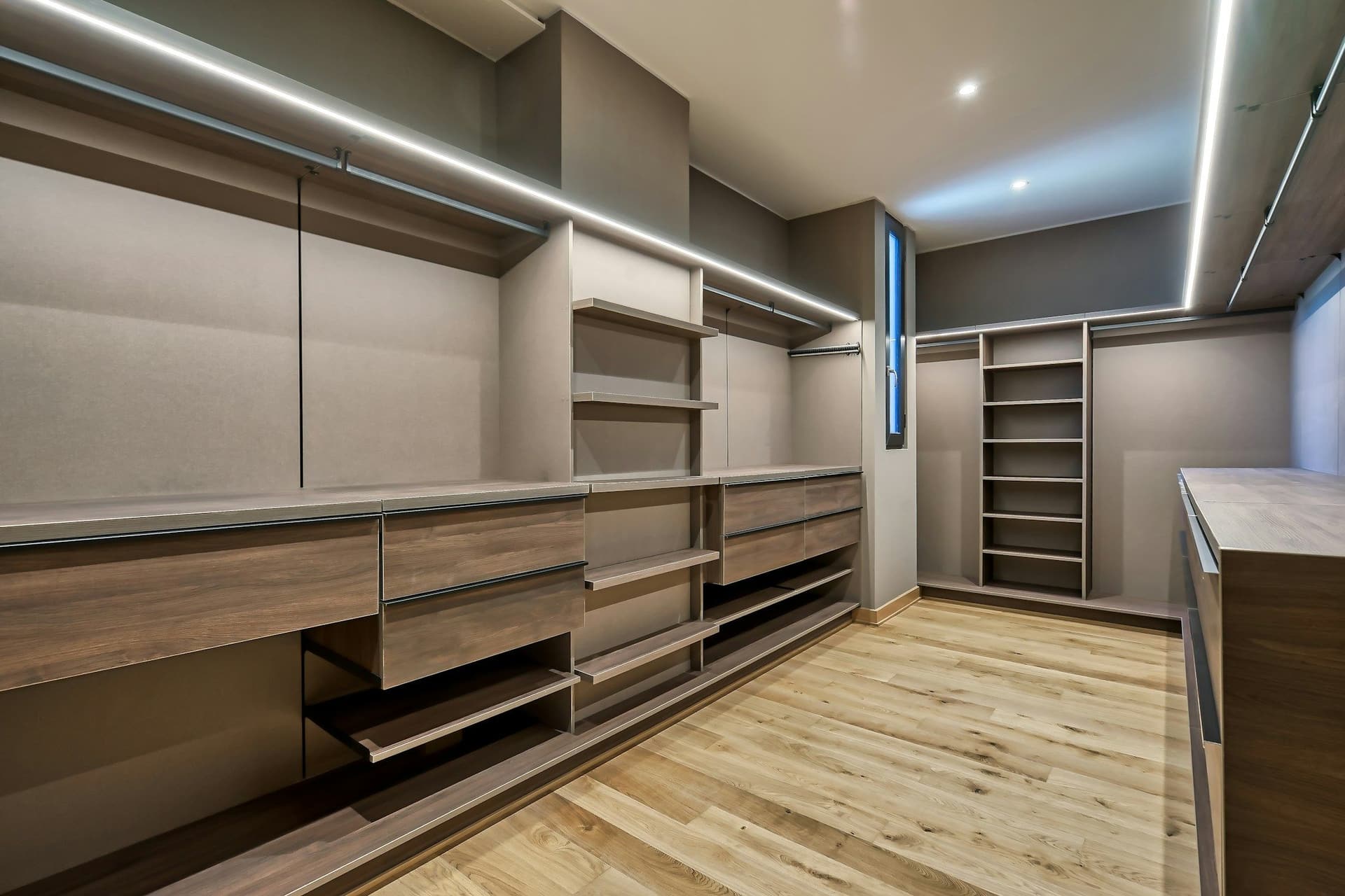 Large walk-in closet with timber-toned drawers, LED strip lighting and a wide-plank floor