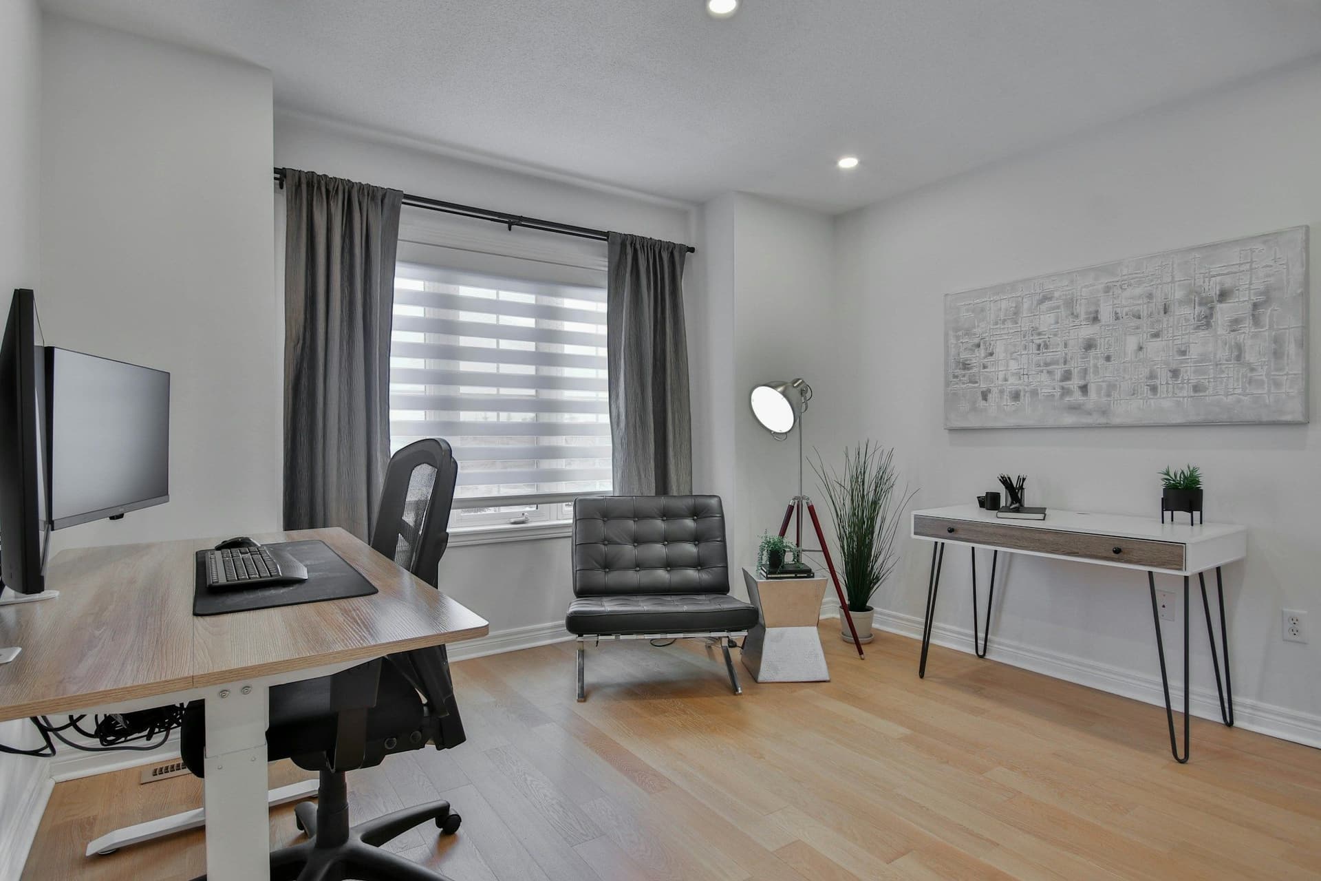 Light home office with a desk and monitor, a leather armchair, a slim side desk and a window blind