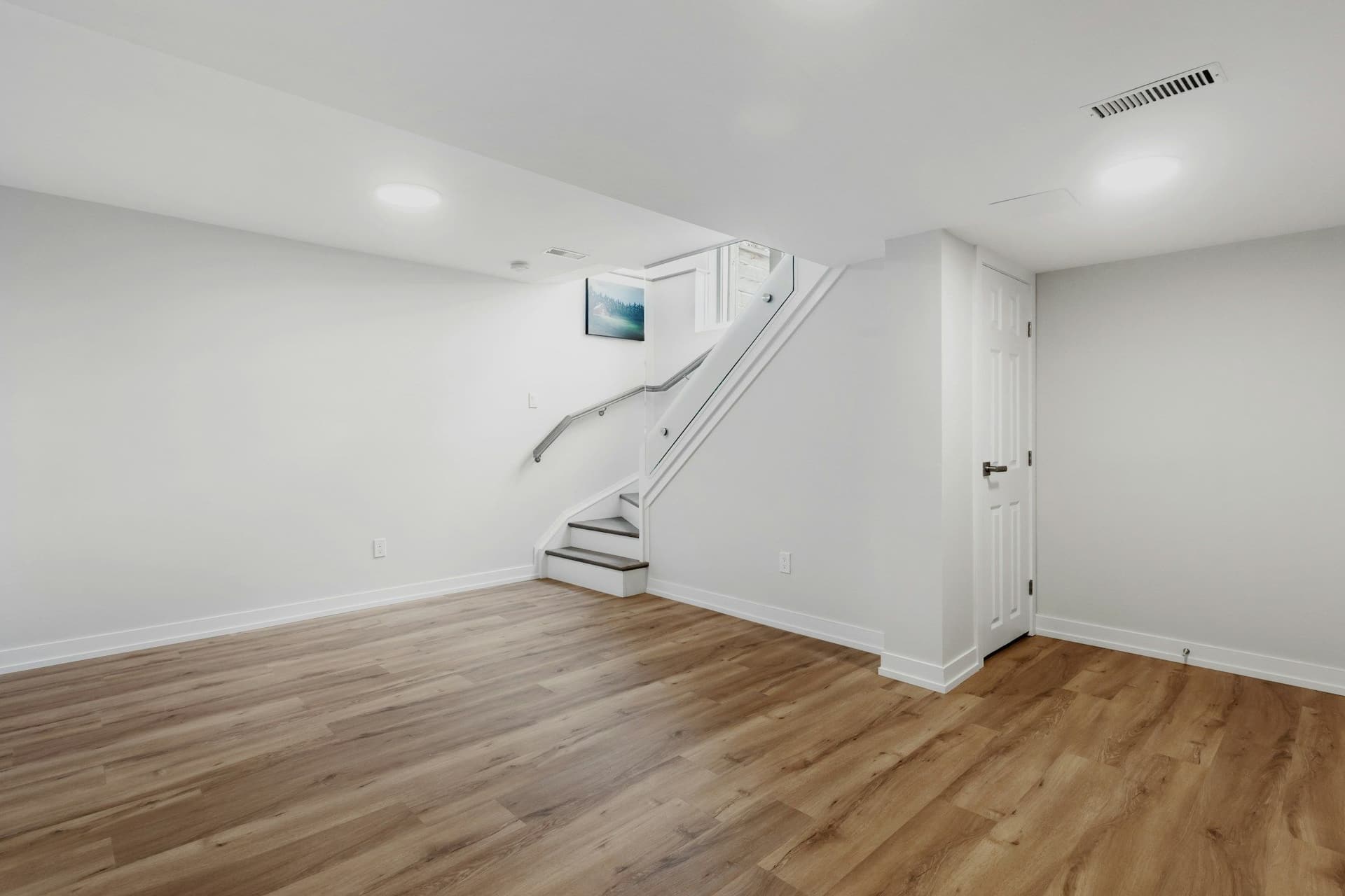 Finished basement with white walls, a wood-look floor and a staircase going up to the floor above