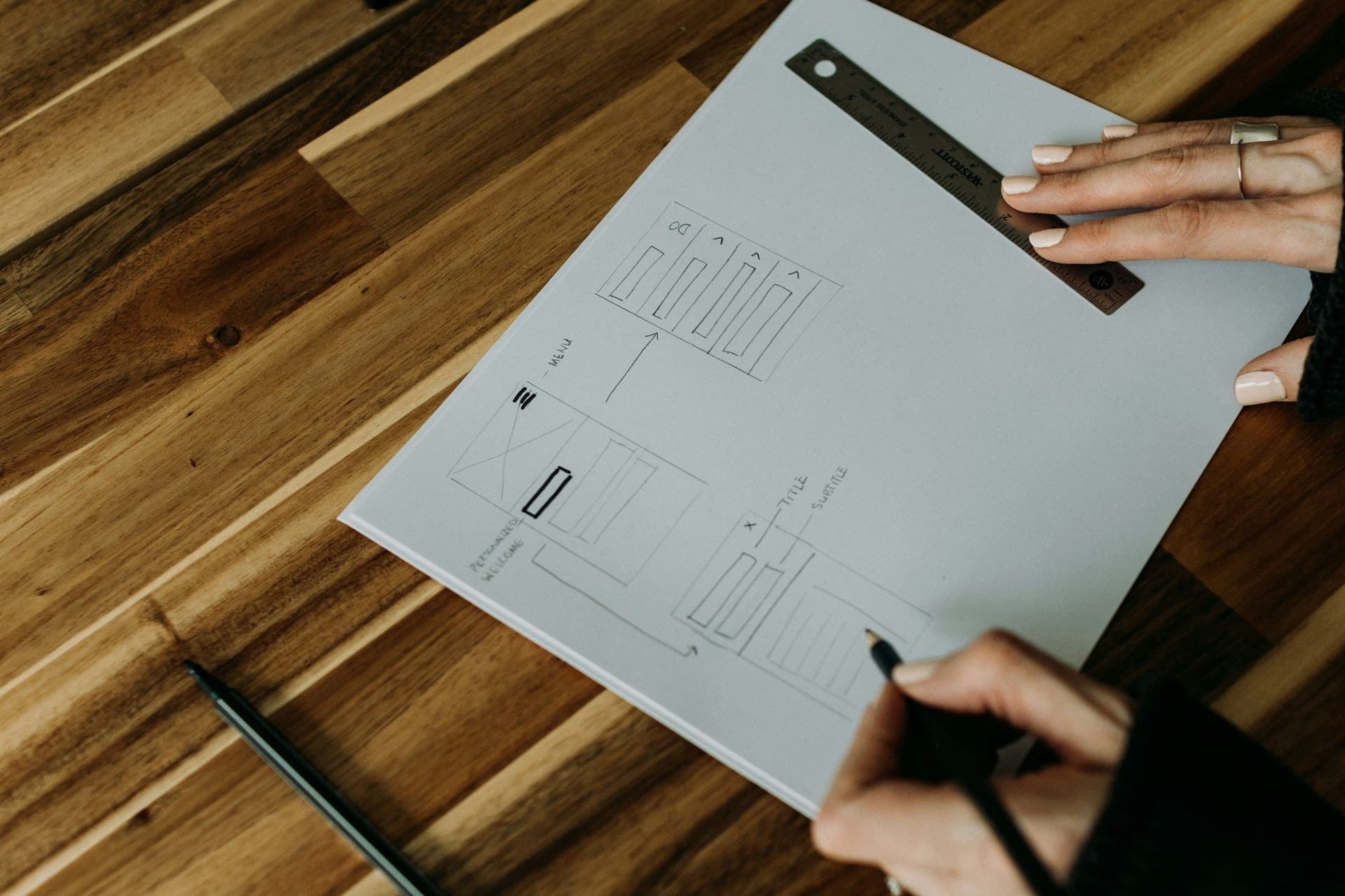 Hands drawing a room plan on paper with a metal ruler on a wooden table