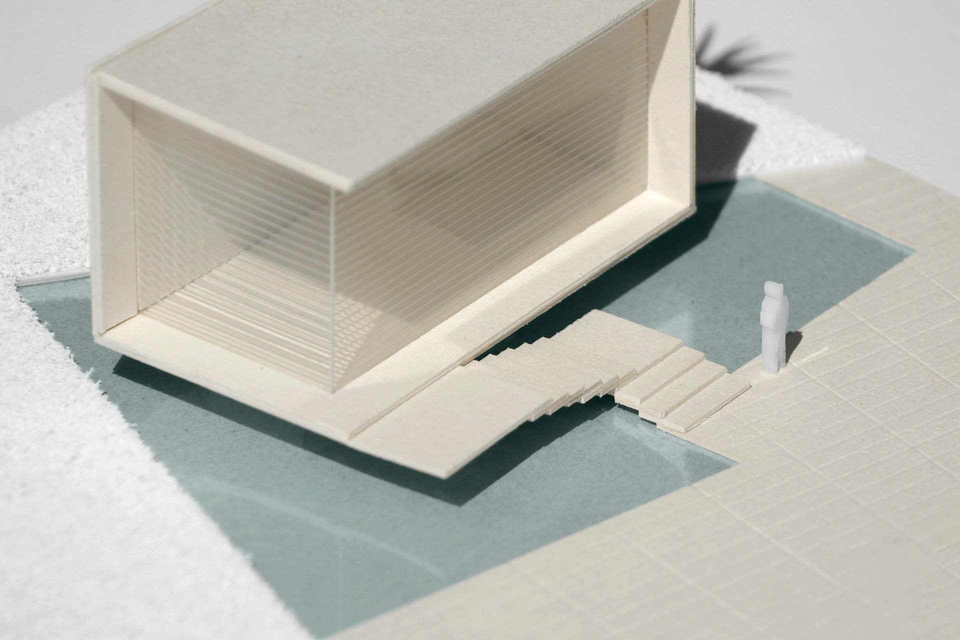 A white architectural model of a modern house with open sides on a pale teal base