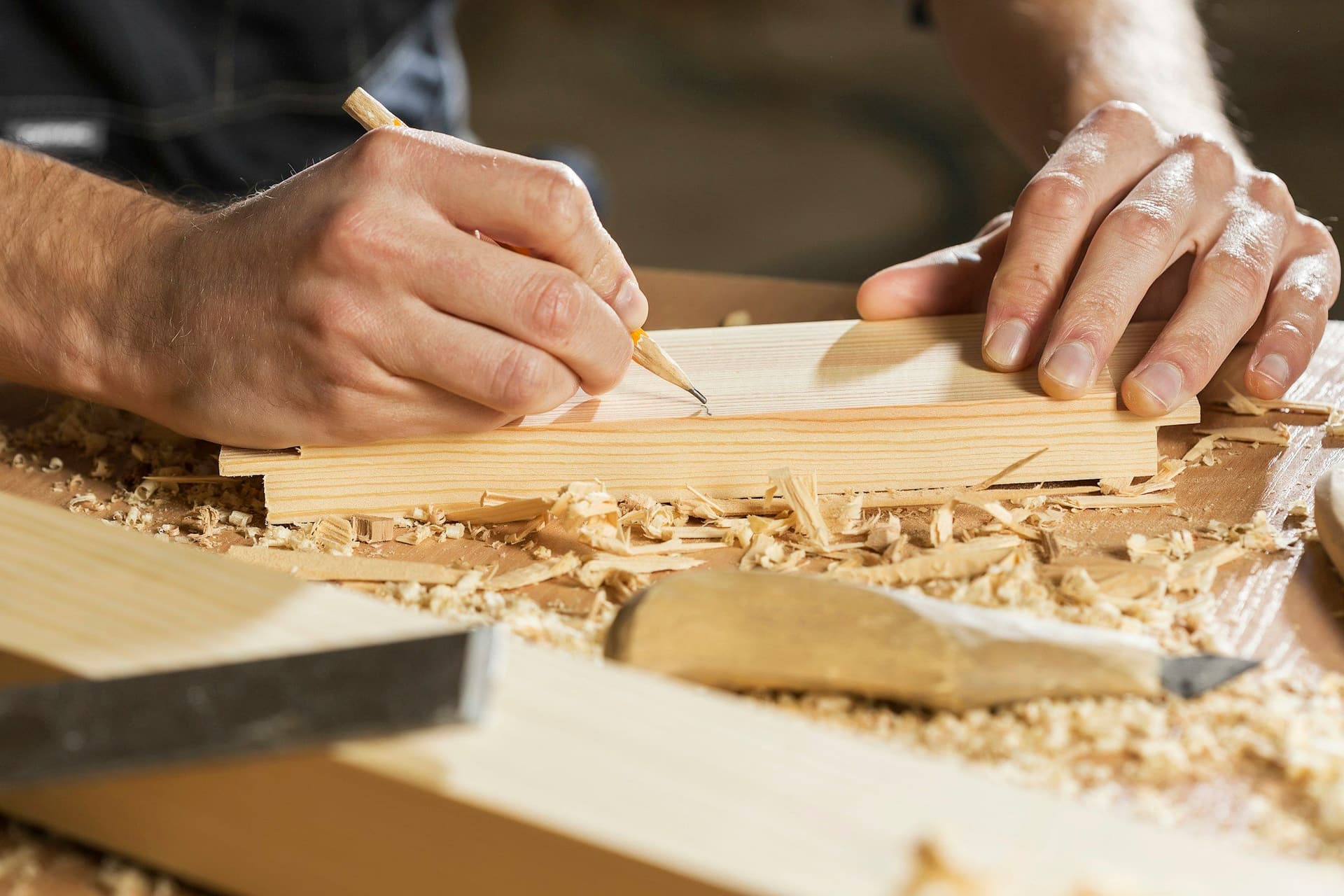 Hands marking a line on a wooden board with a pencil among wood shavings