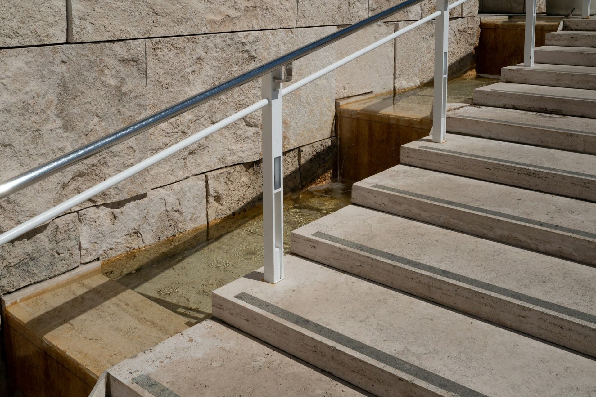 Stone entrance steps with anti-slip strips and a metal handrail alongside