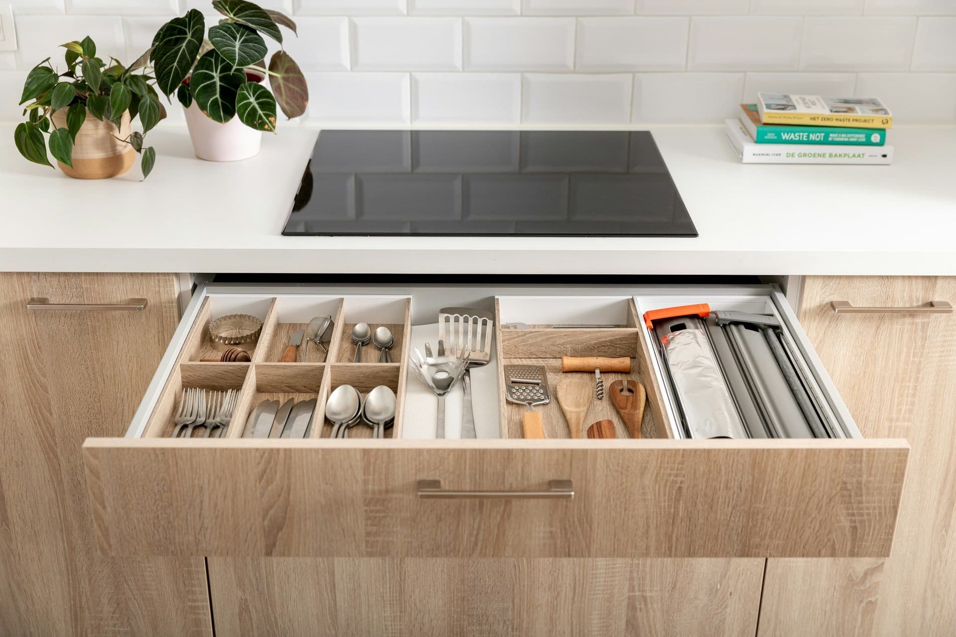 Deep kitchen drawer pulled open beneath a cooktop, fitted with dividers for cutlery and utensils