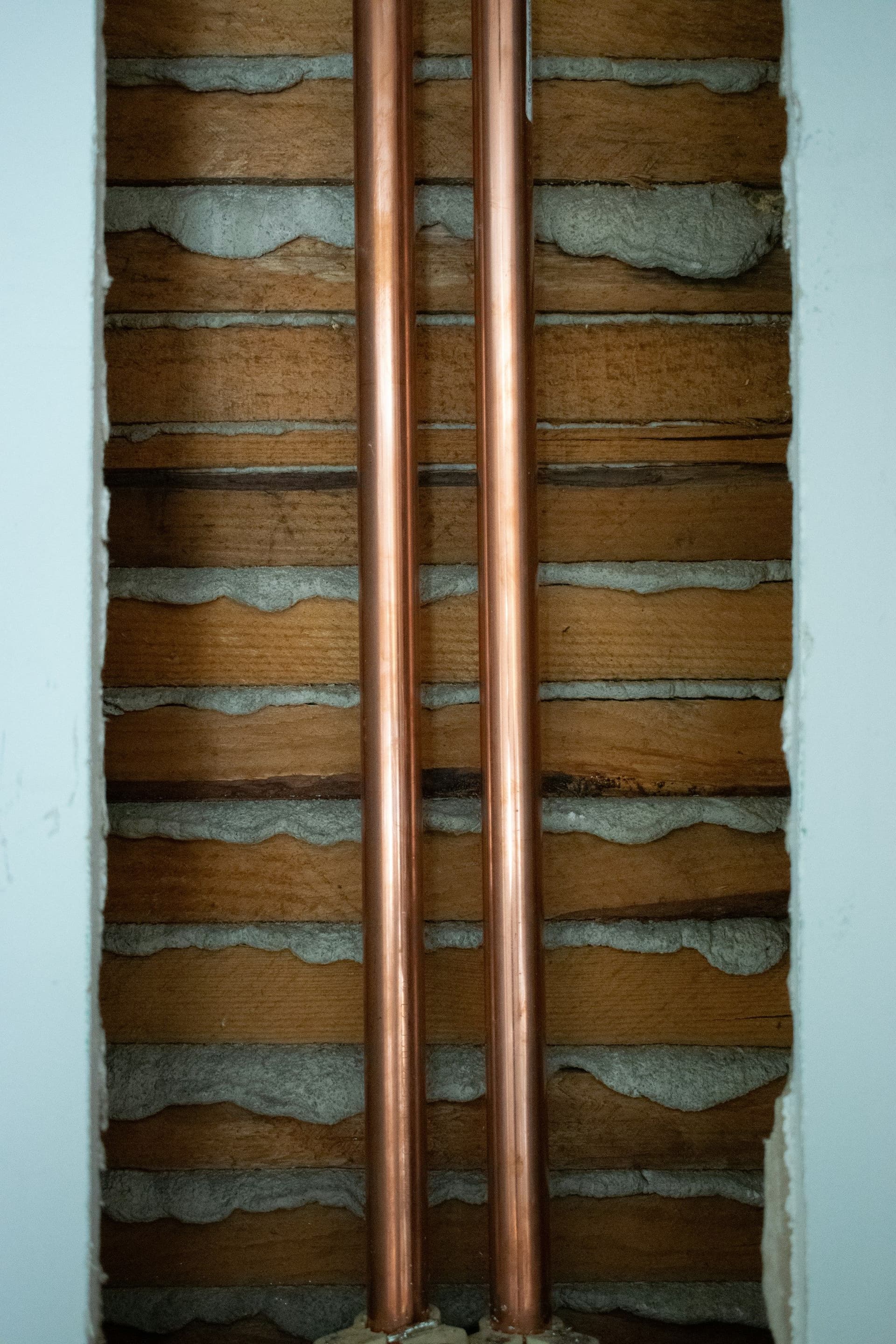 Two copper pipes running up the inside of an opened wall between exposed timber battens