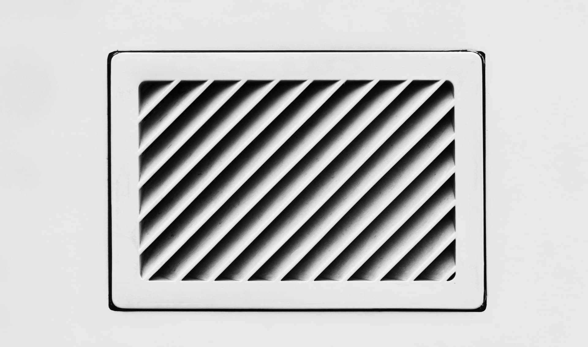 White rectangular vent grille with diagonal slats set in a plain white wall