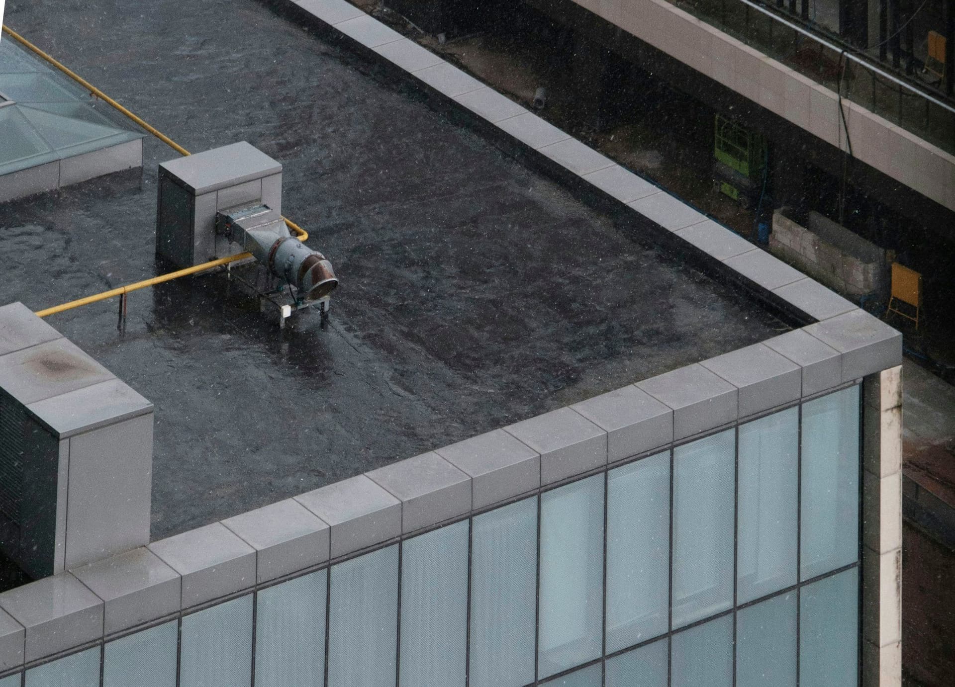 Dark waterproofed flat roof with stone coping around its edge and a pipe vent, seen from above