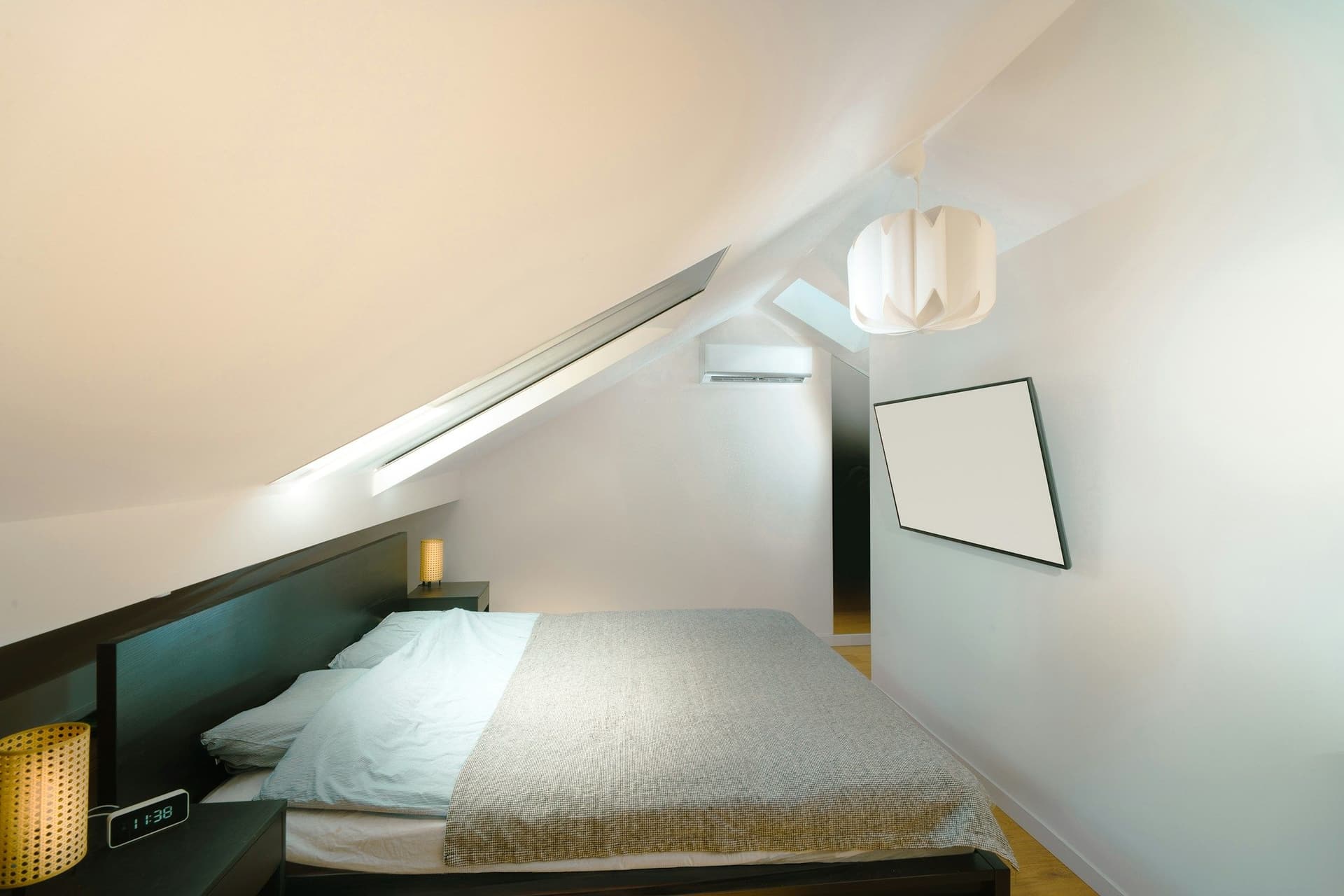 Bedroom under a sloped ceiling with a low bed, a wall-mounted air conditioner and a paper pendant light