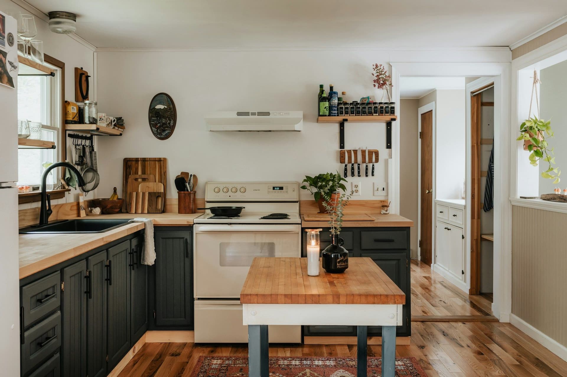 Kitchen with dark green cabinets, timber countertops and a small timber-topped island on a wood floor