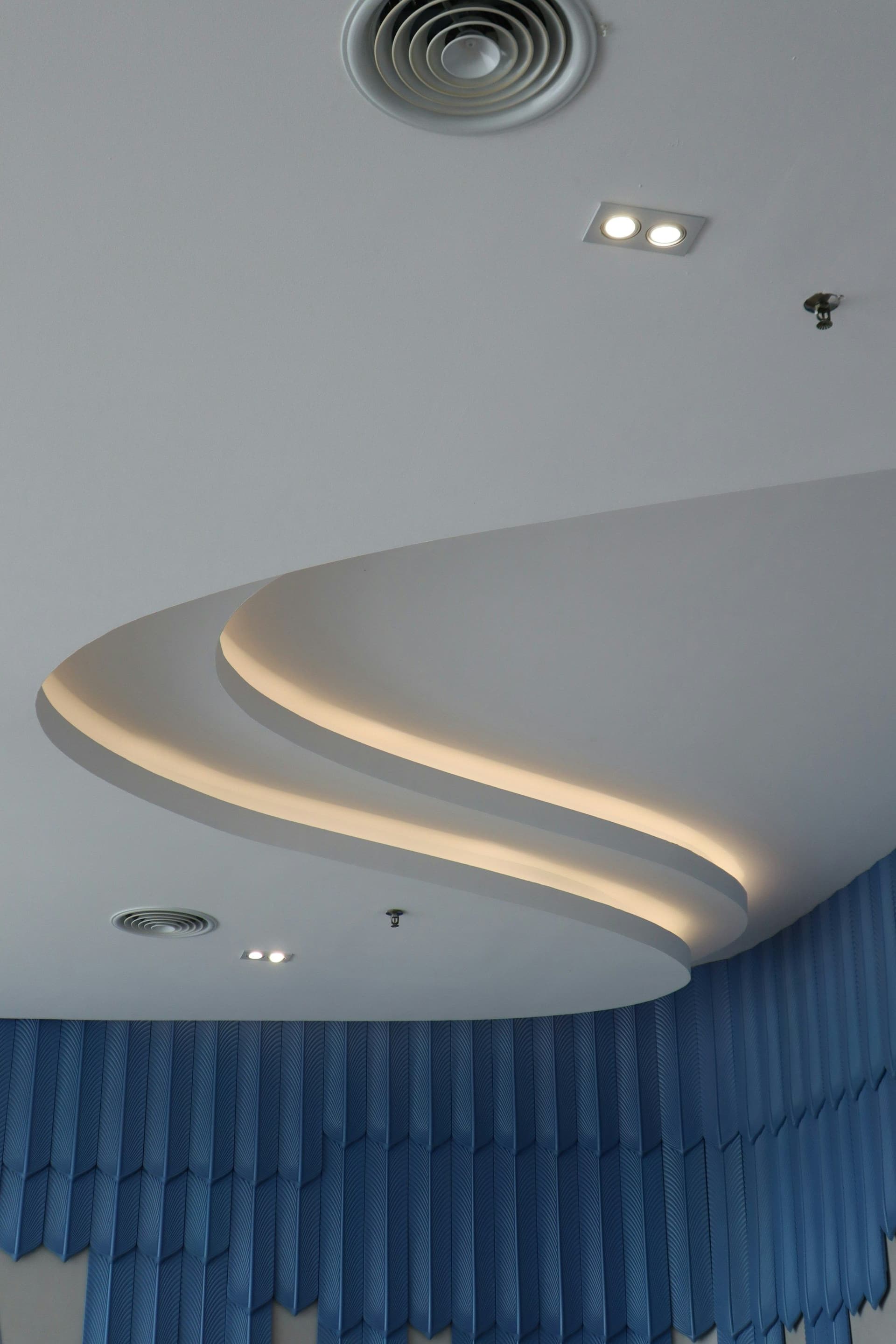 Curved white ceiling edge with a glowing light strip, an air vent and blue drapes below