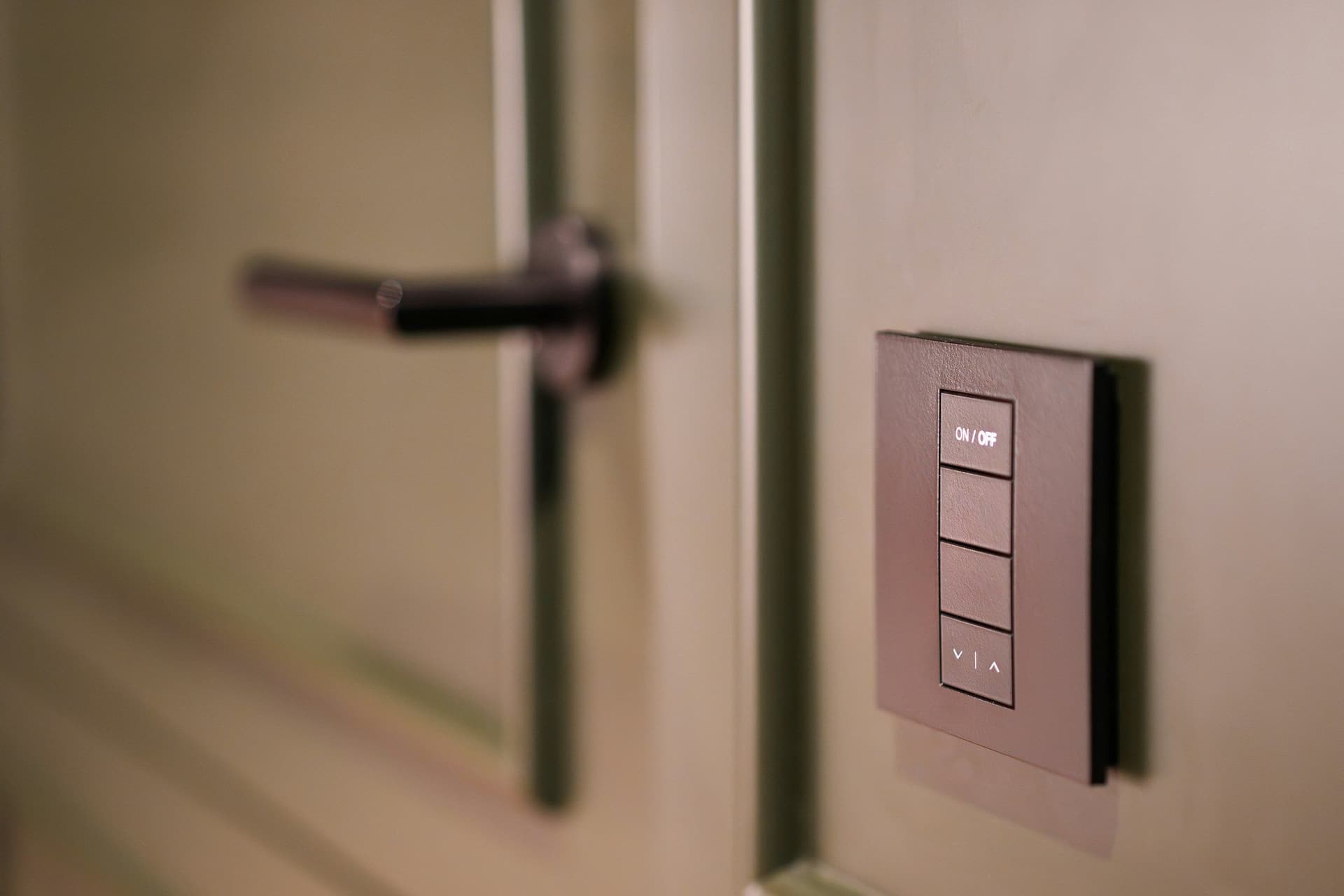 Brown wall keypad with four buttons for lighting scenes, mounted beside a door handle