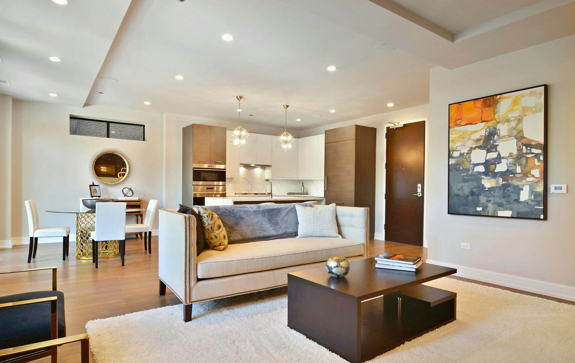 Open living and dining space with a cream sofa, a dark coffee table, an abstract painting and a kitchen beyond