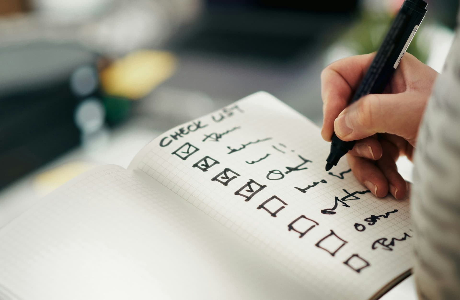 A hand ticking boxes on a handwritten checklist in an open notebook