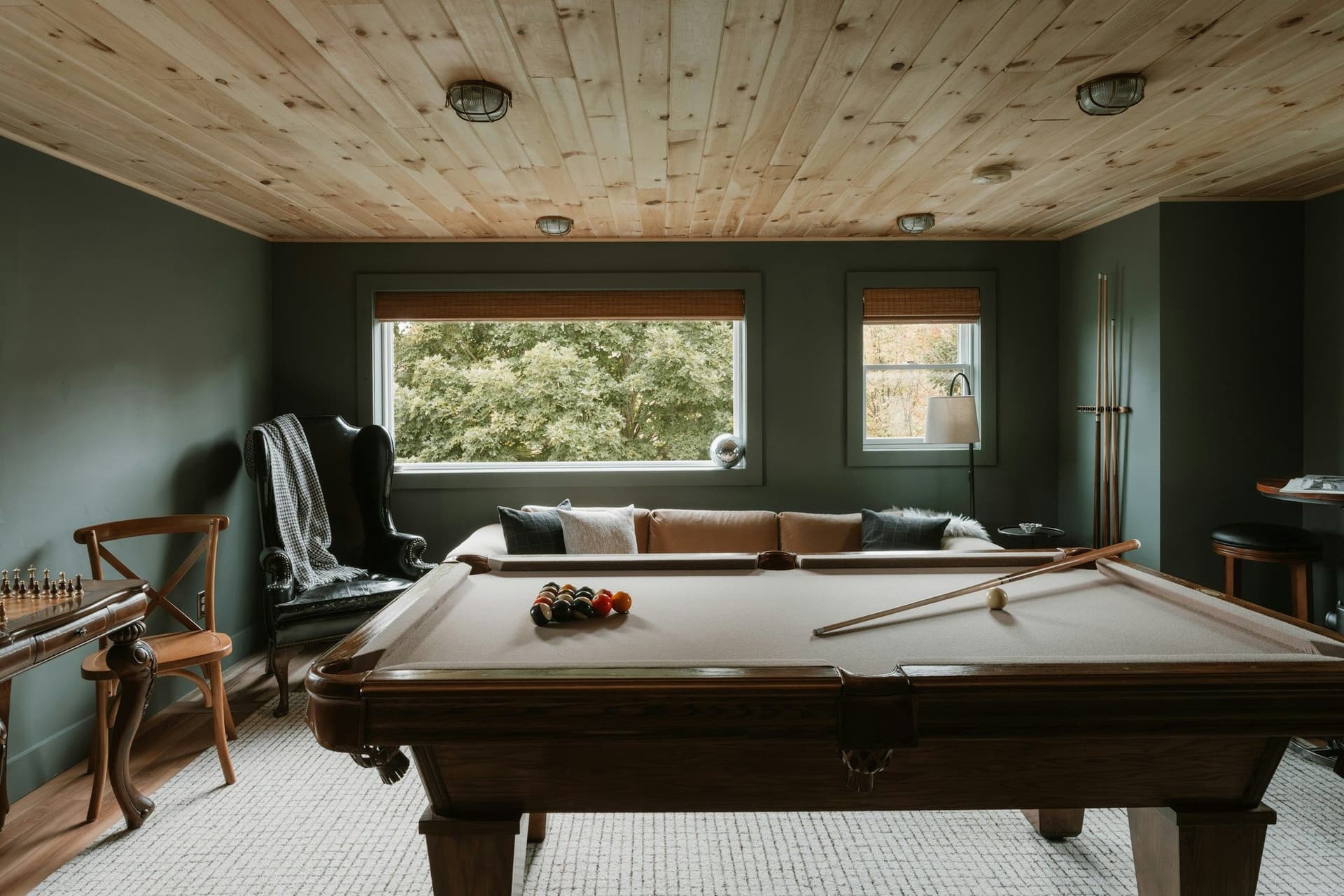 Game room with a pool table, armchairs, green walls and a wood-plank ceiling