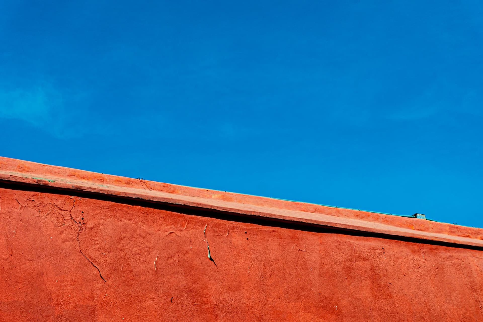 Sunlit terracotta-red rendered wall edge against a deep blue cloudless sky