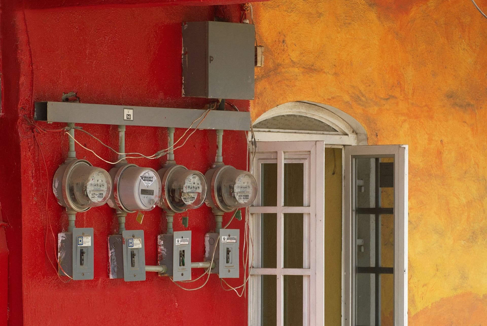 Four electricity meters with switches mounted on a red wall beside an arched window