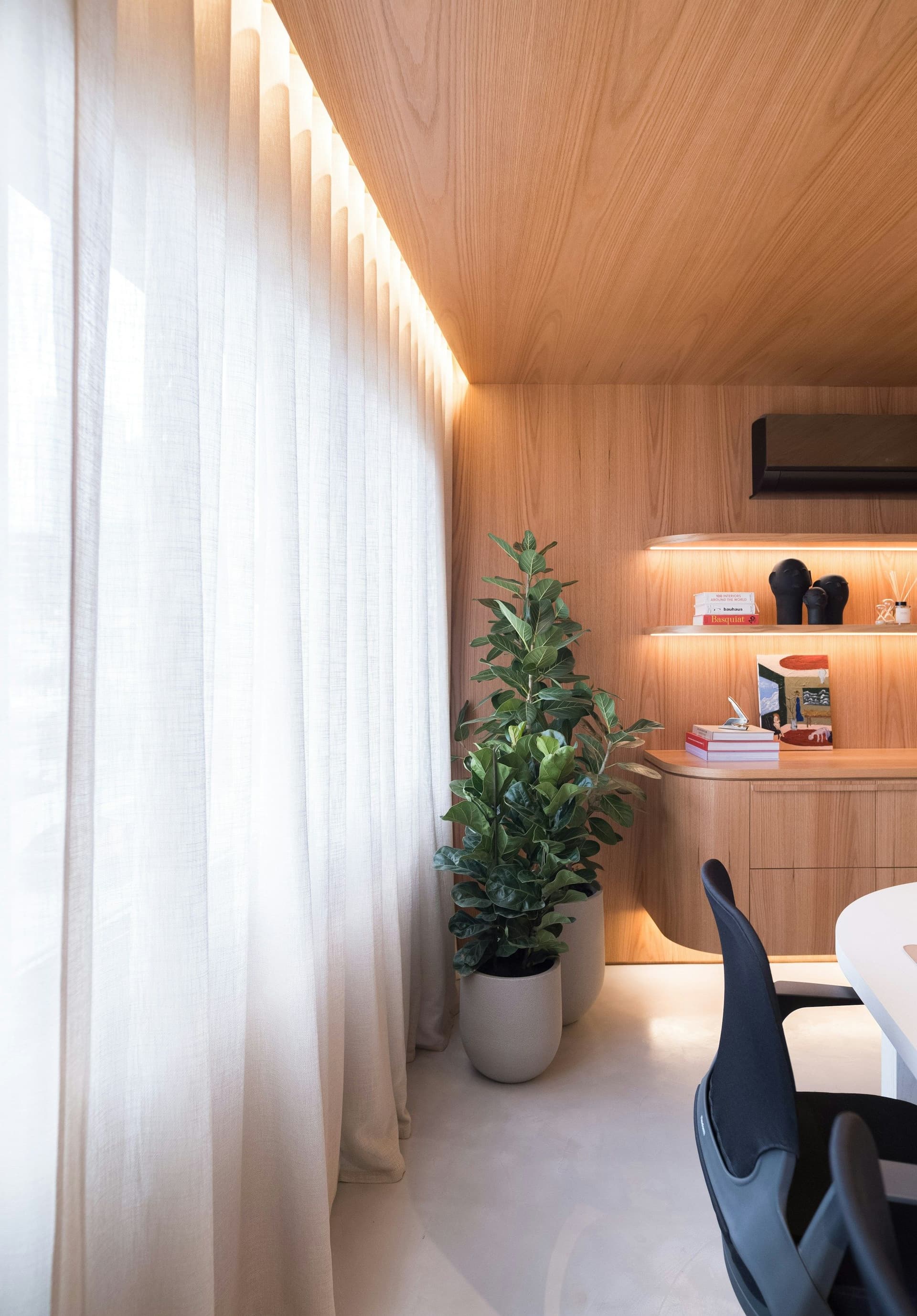 Wood-paneled room with a wood ceiling, sheer curtains, a wall-mounted air conditioner, lit shelves and a potted plant