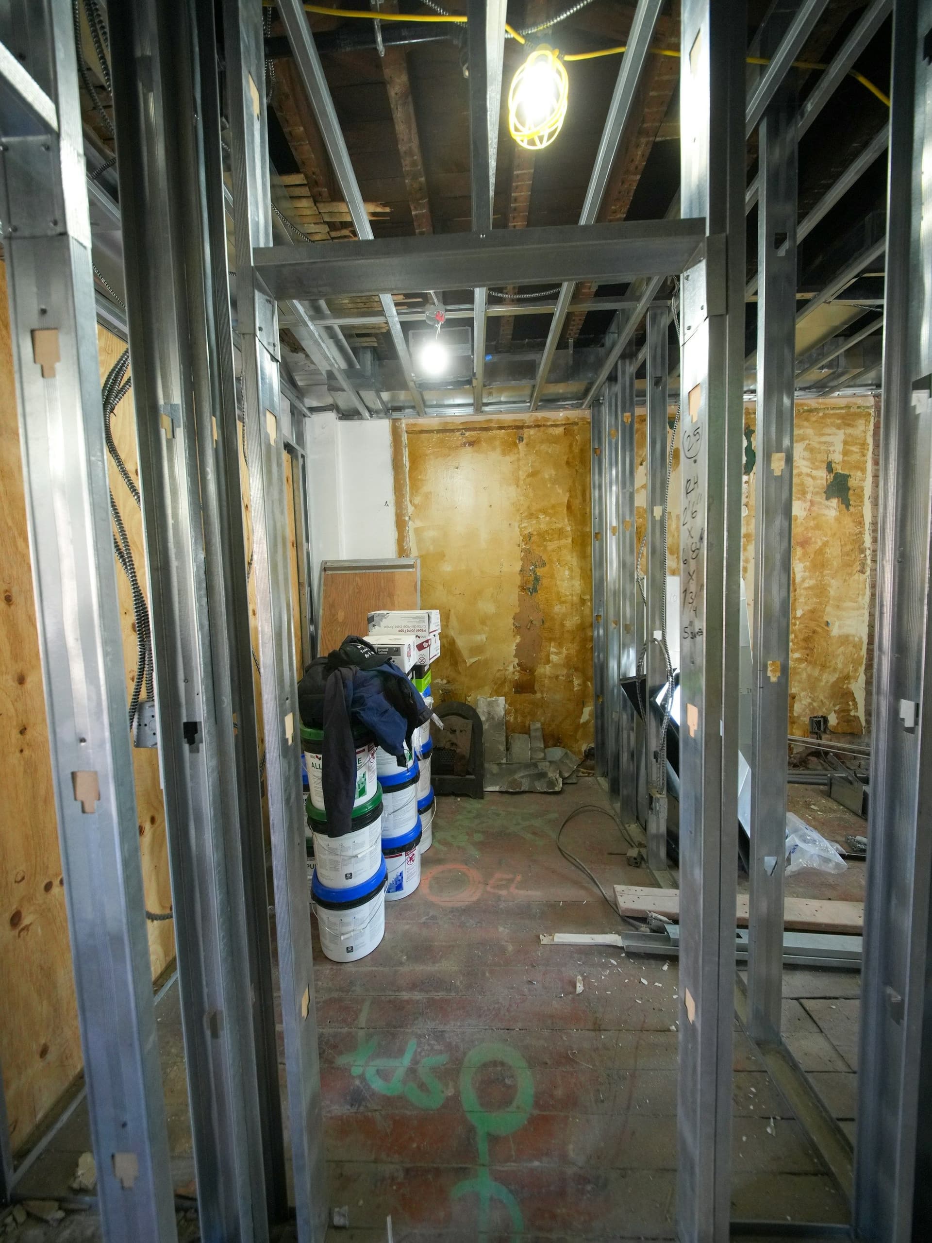 Metal stud framing, bare ceiling joists and stacked paint buckets in a hallway being renovated