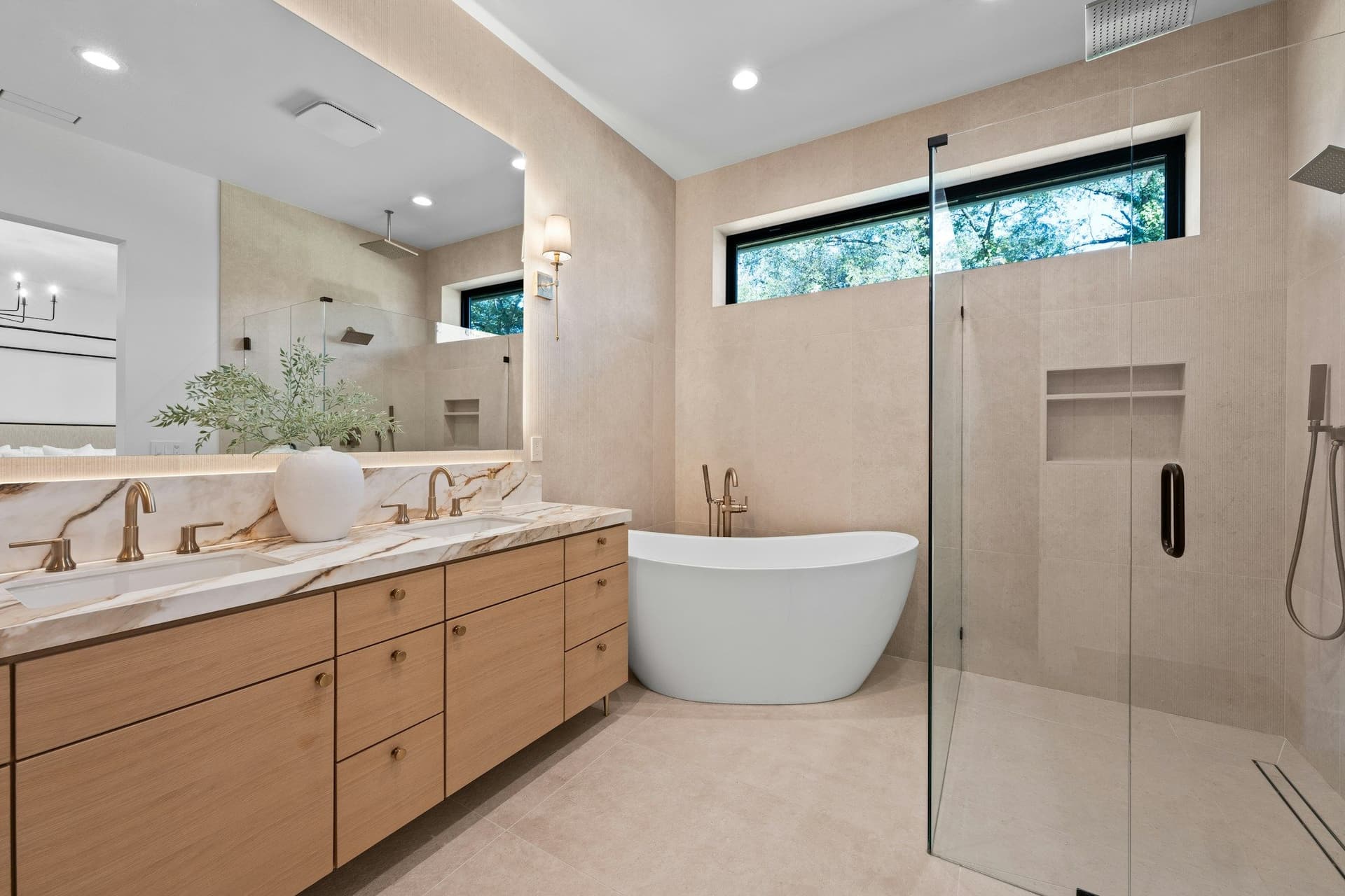 Bathroom with a wood double vanity, a freestanding bath, a glass-walled shower and a high window