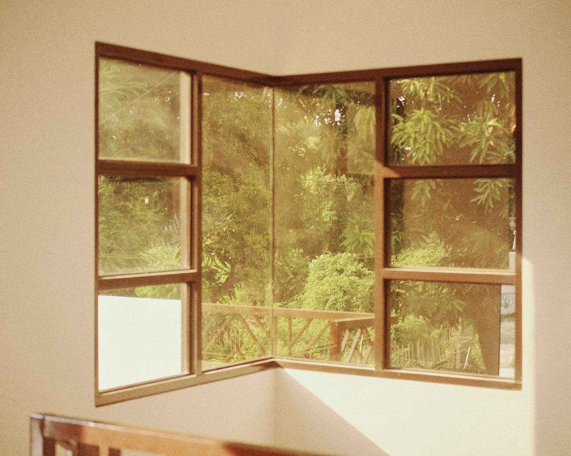 Corner window with timber frames opening onto trees and a balcony railing