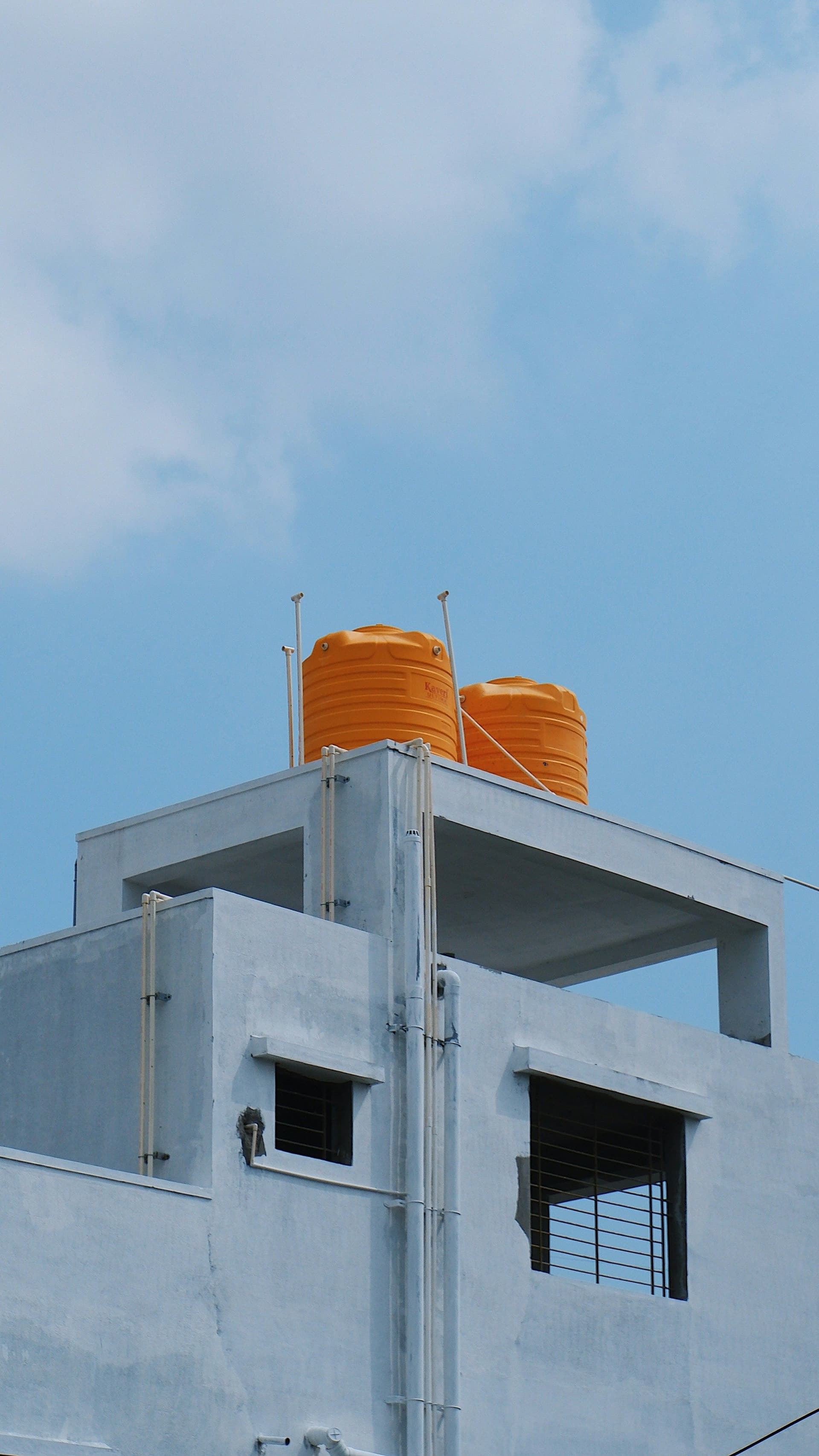 Two orange water tanks on the flat roof of a pale blue building under a blue sky