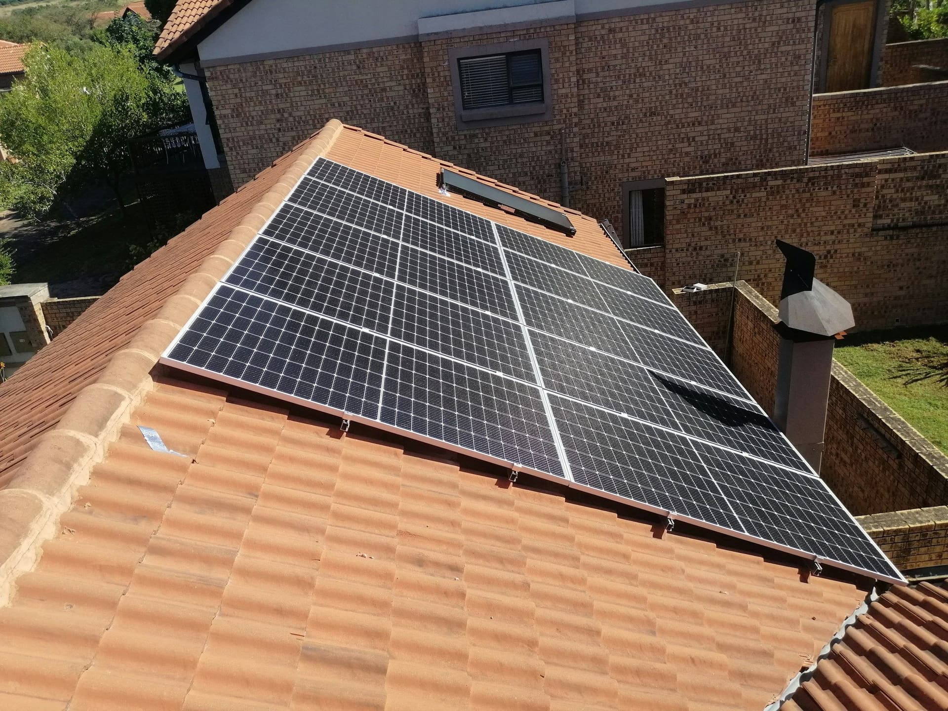 Black solar panels installed on a terracotta tiled pitched roof beside a brick house wall