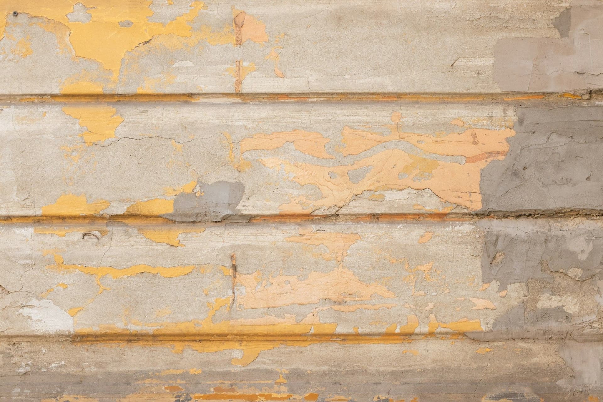 Rendered wall with horizontal grooves and patches of peeling yellow paint over gray concrete