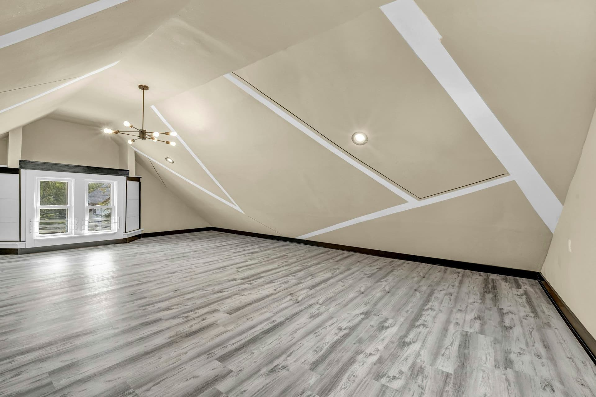 Finished attic room with sloped ceilings, a wood-look floor, a chandelier and windows at the far end